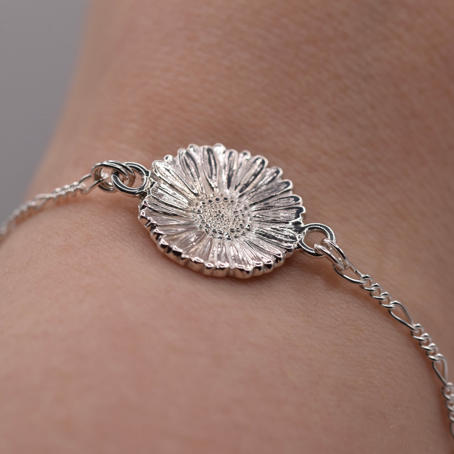 Silver bracelet with a daisy shaped motif on a wrist against a neutral background