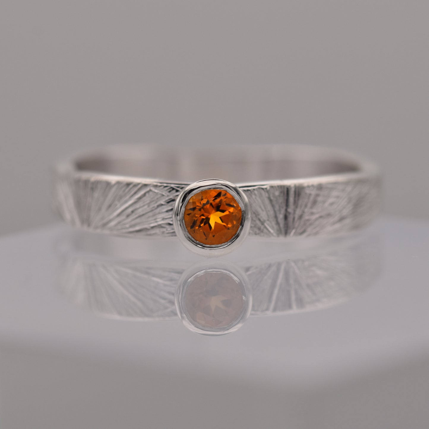 Silver patterned ring with a round orange/yellow citrine gemstone on a gray background