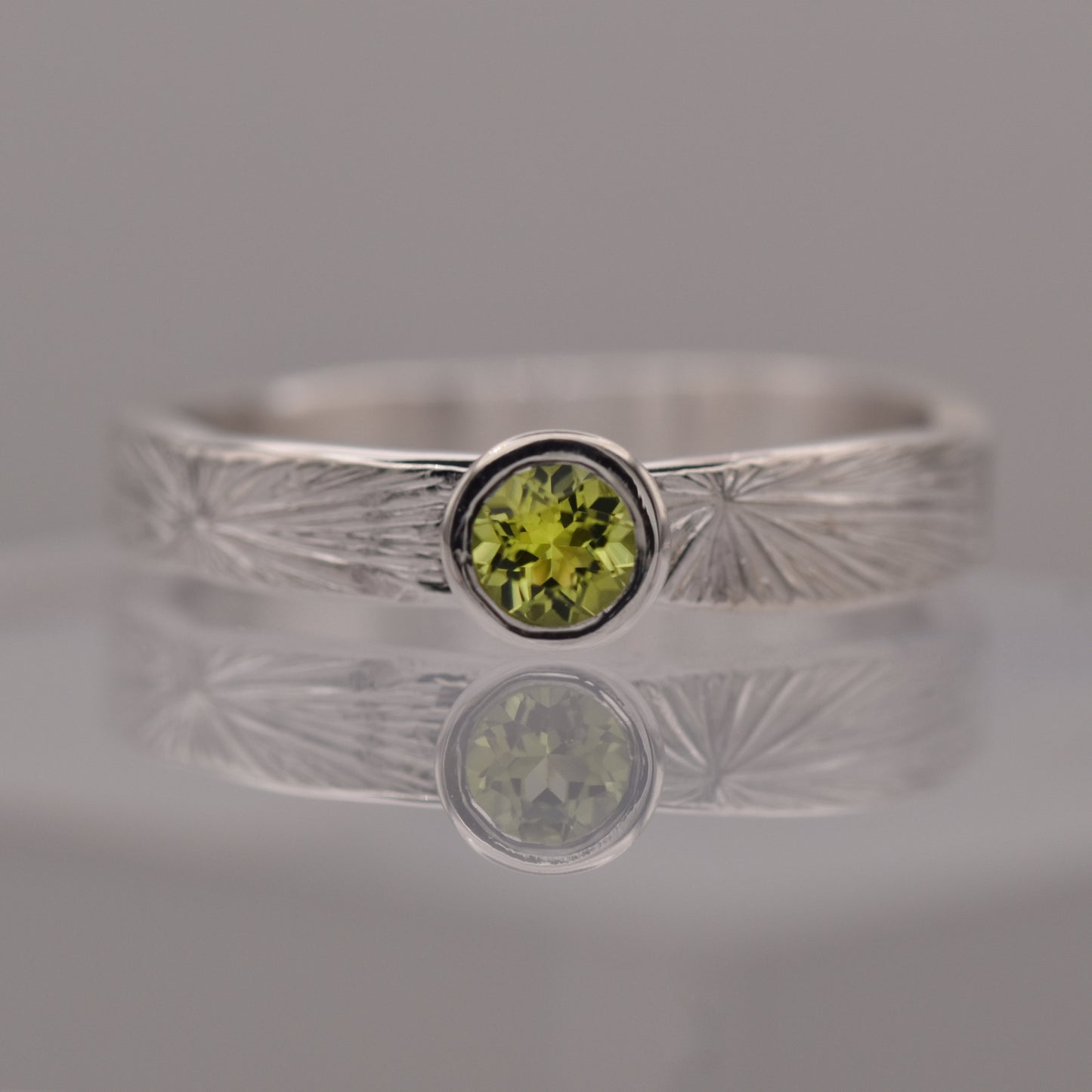 Silver ring with a green gemstone on a reflective surface