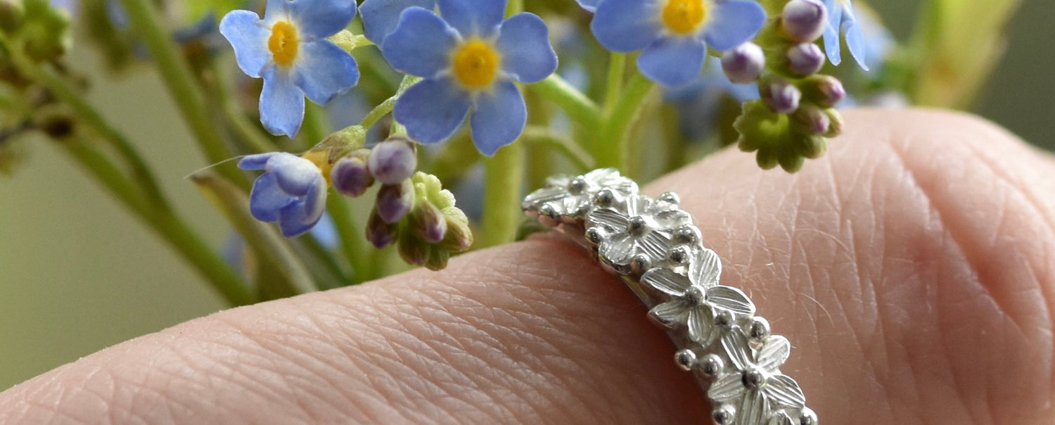 Silver ring on a finger with blue flowers in the background