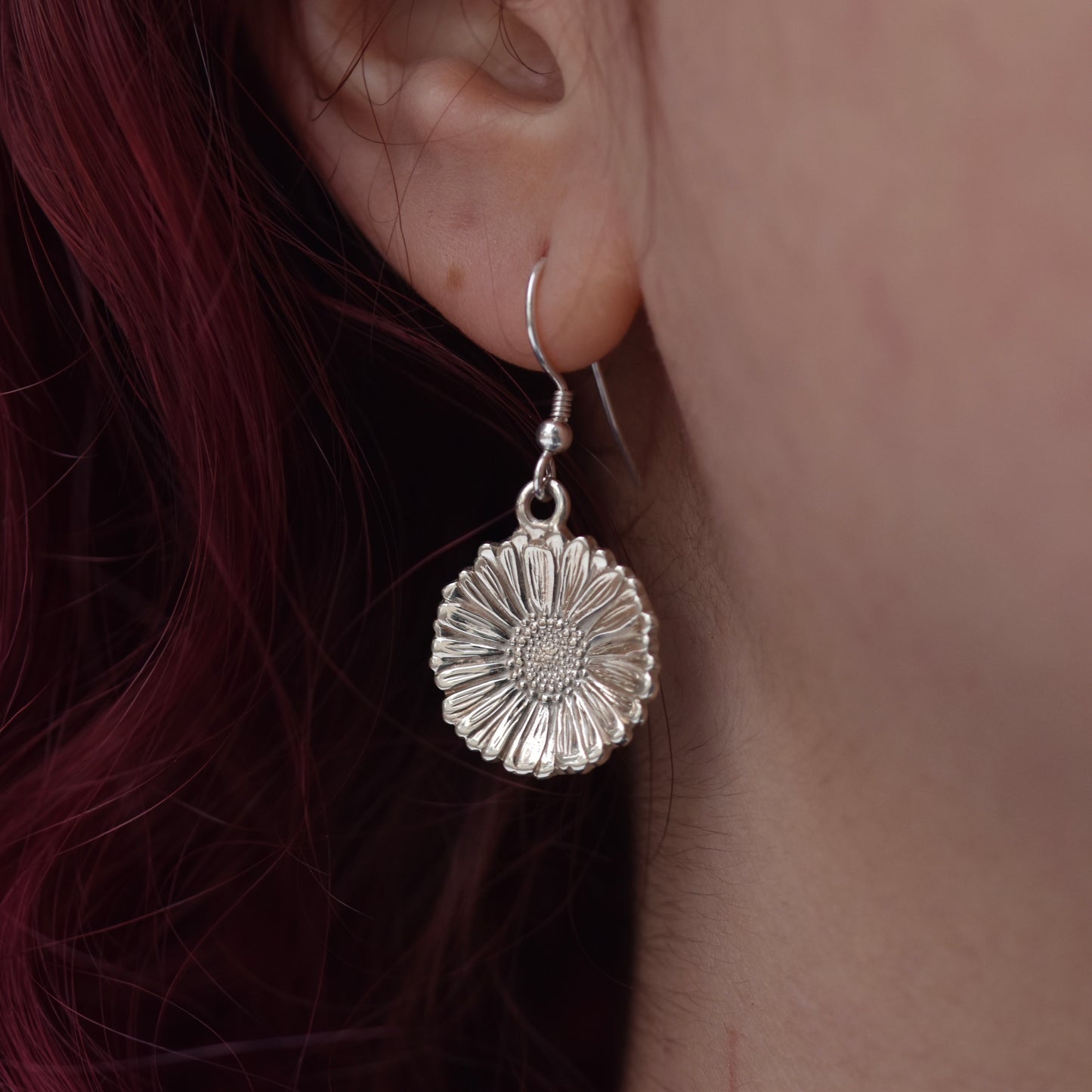 Beautiful sparkly highly detailed and realistic daisy earring on silver hook. Hanging on an earlobe worn by a girl with red hair.