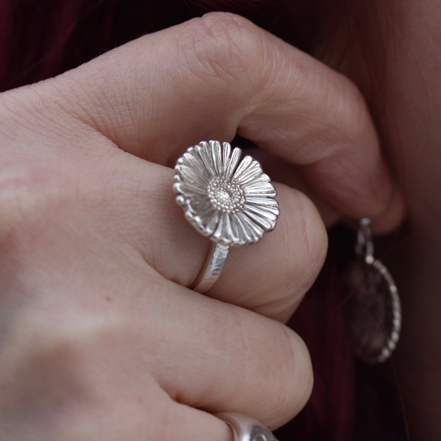 Girl with red hair putting on her earrings wearing a realistic highly detailed Daisy ring made of shiny silver on her middle finger.