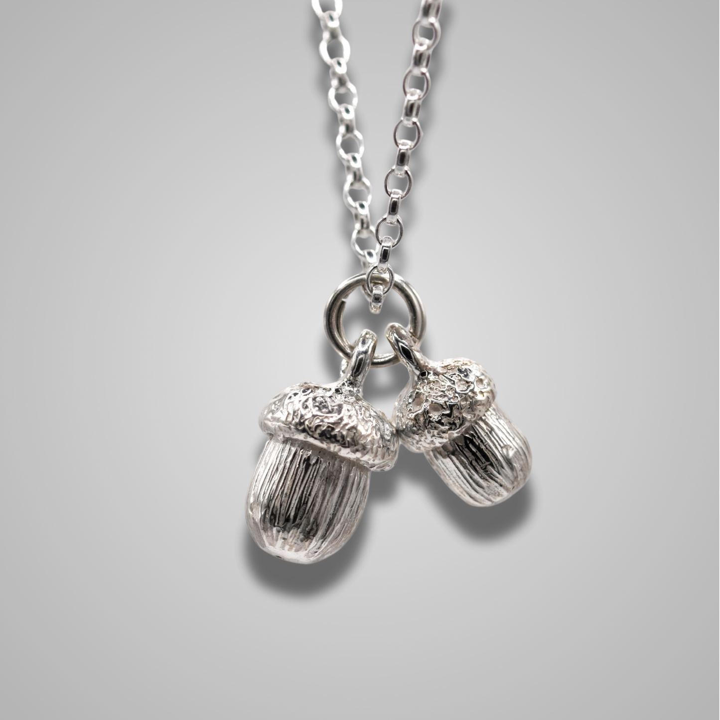 Sterling silver acorns pendant. One large and one slightly smaller nestled beside each other on a jump ring. Intricately detailed , elegant and delicate