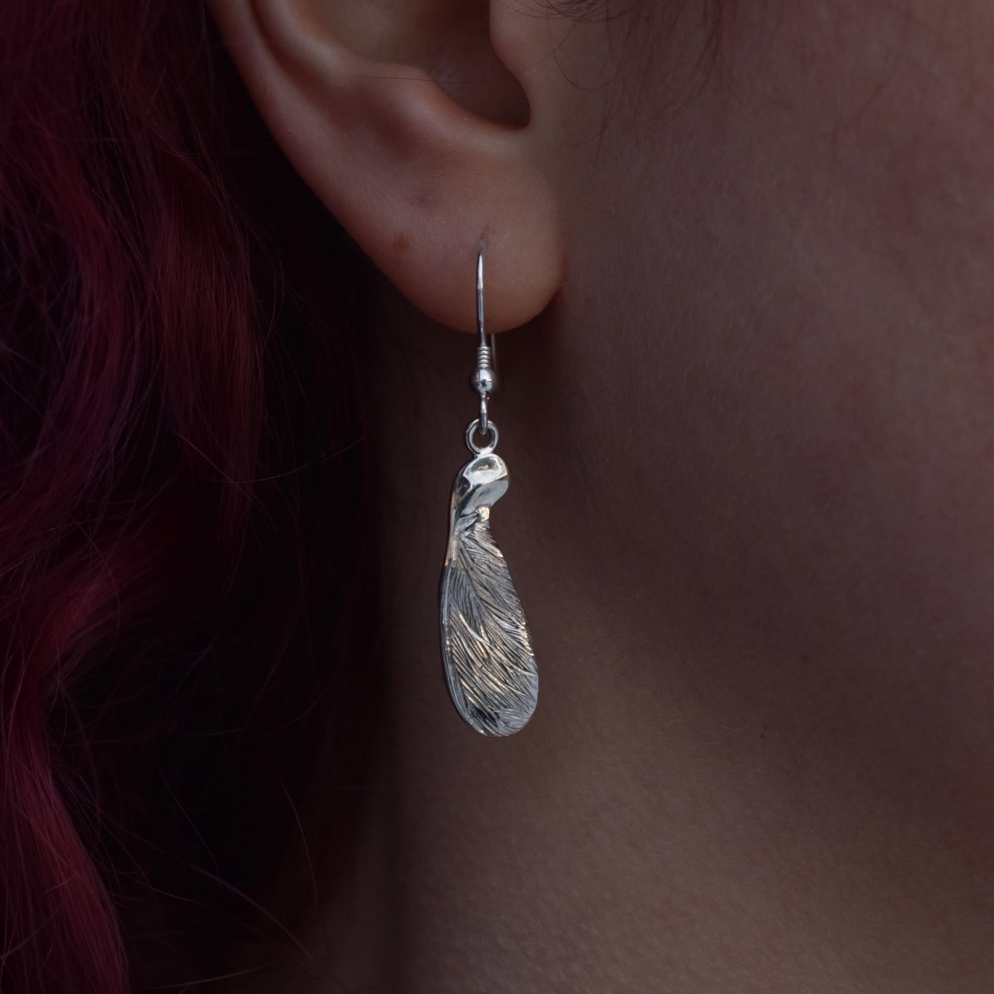 Girl with red hair wearing a large drop earring representing a highly detailed and realistic half sycamore seed earring made from silver on a silver hook