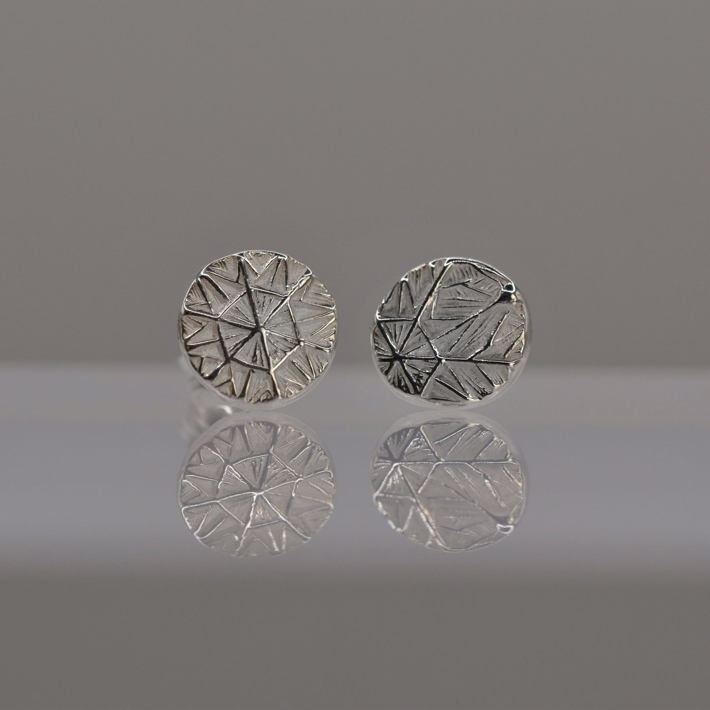 Pair of silver round earrings with textured design of frost pattern on a reflective surface.