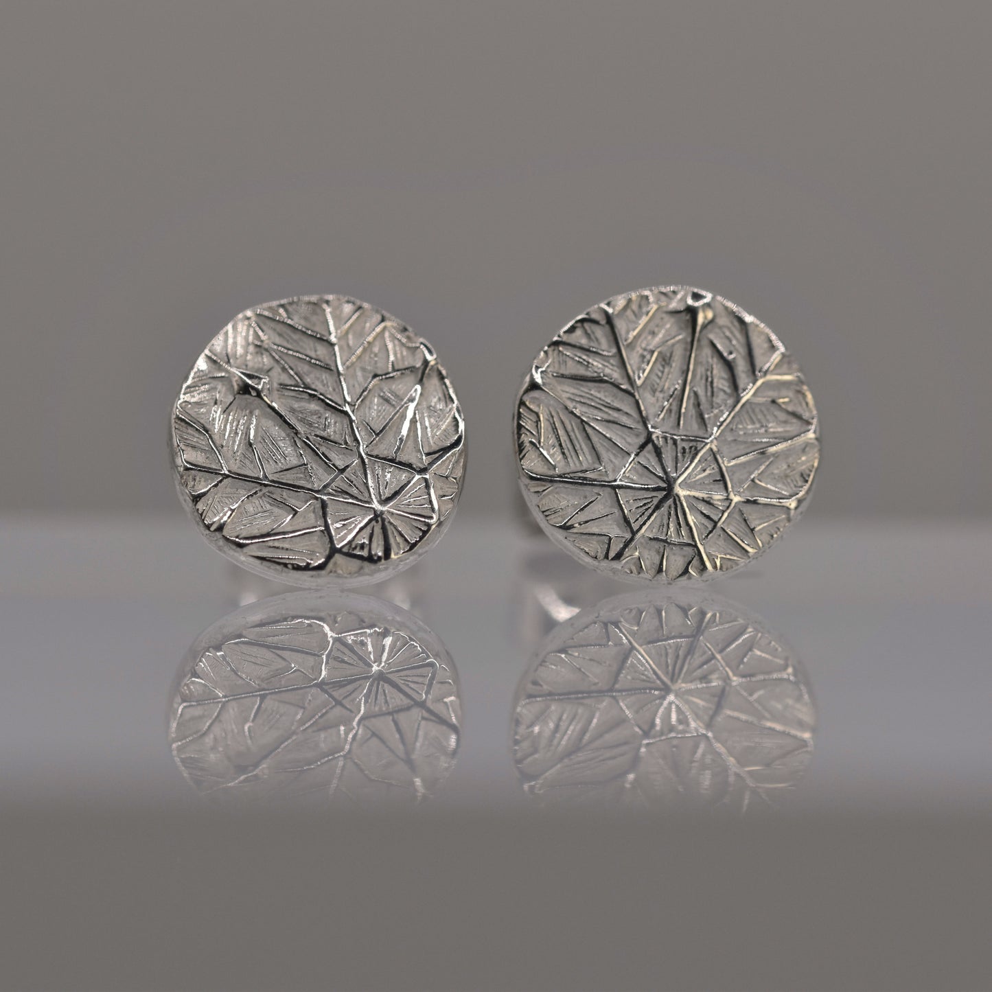 Pair of silver round earrings with textured design of frost pattern on a reflective surface.