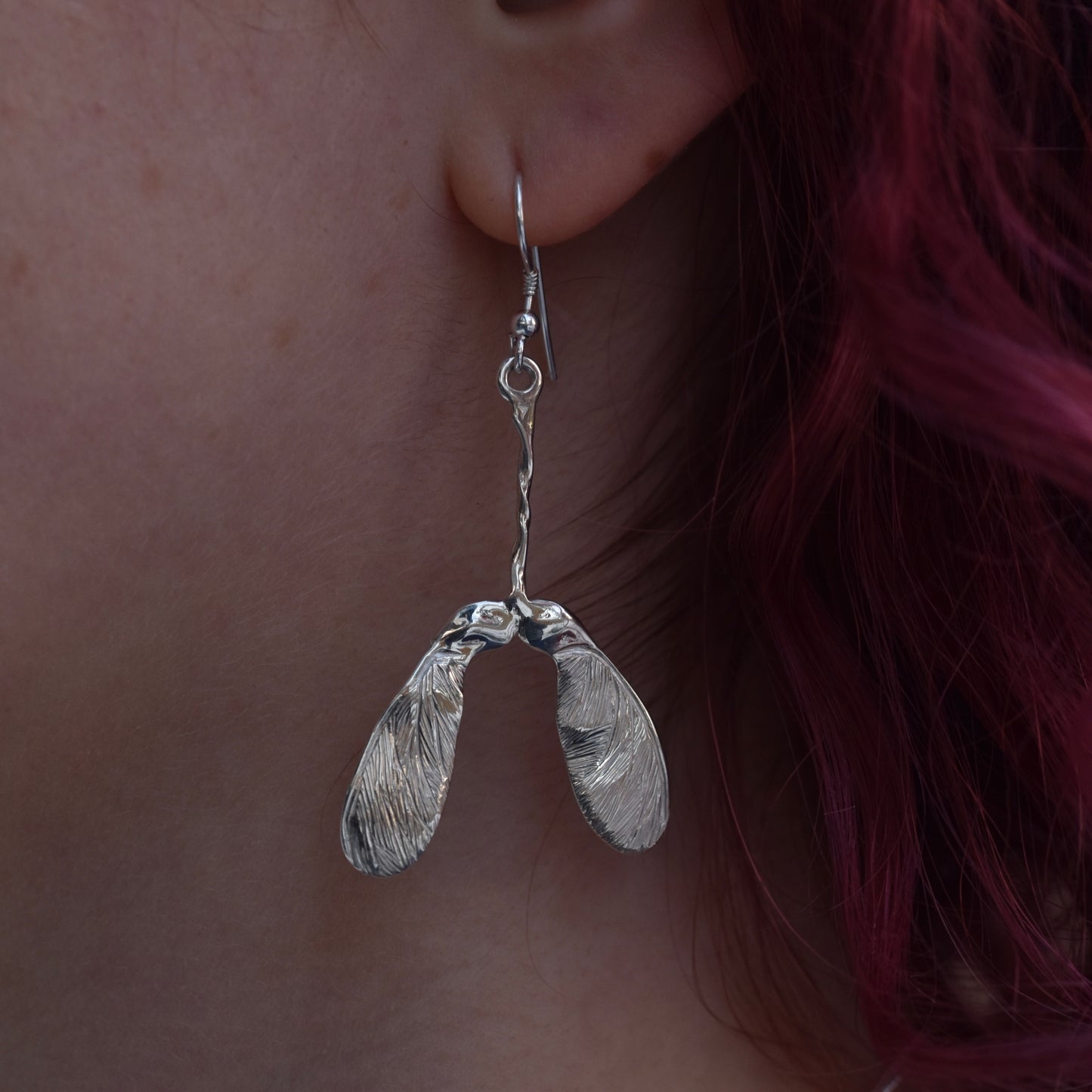 Very shiny earring worn by a girl with red hair. The earring is a sycamore seed covered in sparkles engraving with highly polished silver on a silver hook