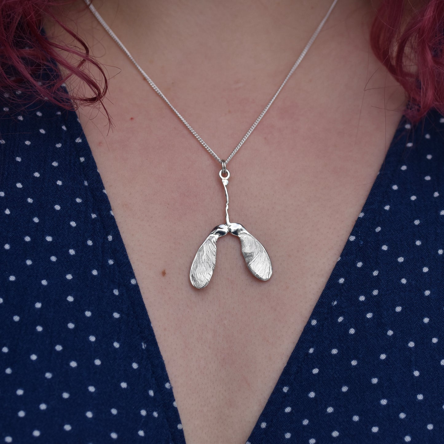 Girl wearing a blue dress is wearing a sycamore seed pendant. The pendant is highly detailed and sparkly with engraved details on a silver chain