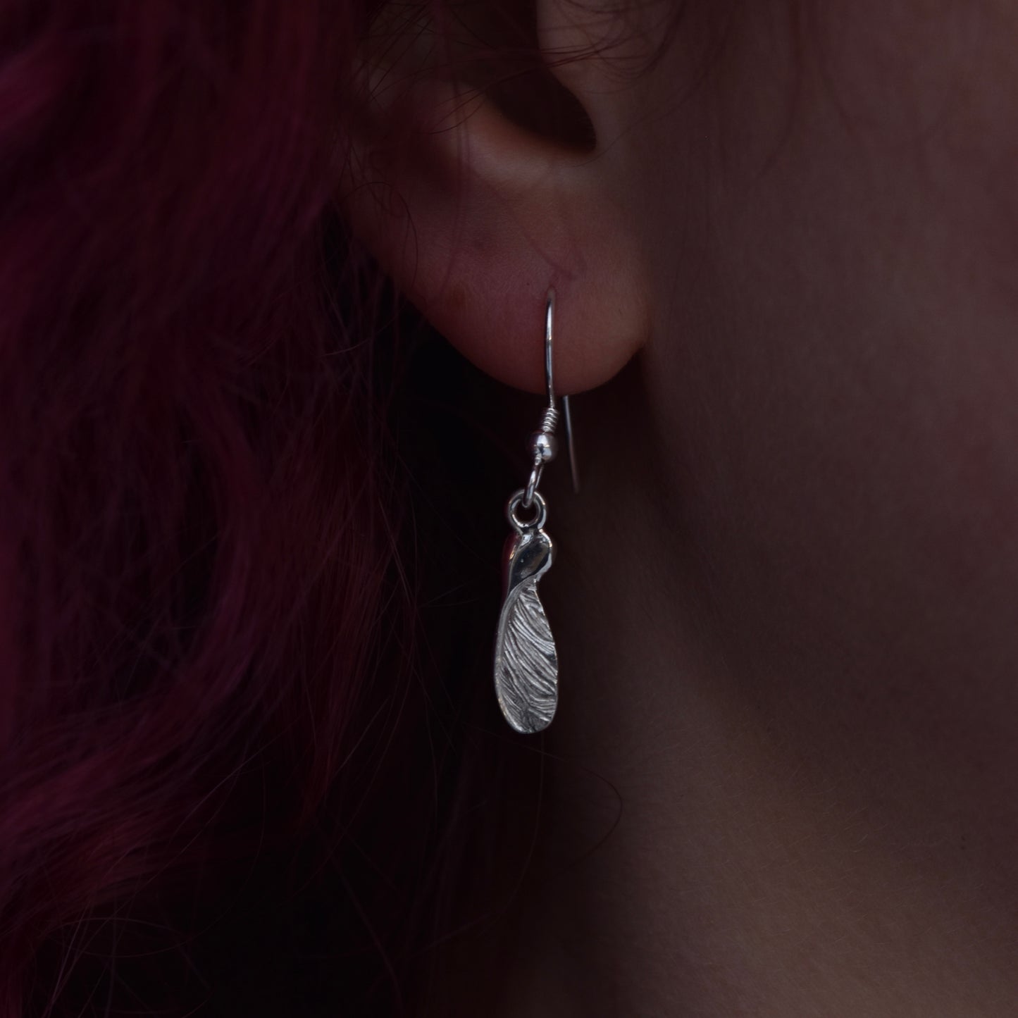 Girl with red hair wearing a medium drop earring representing a highly detailed and realistic half sycamore seed earring made from silver on a silver hook