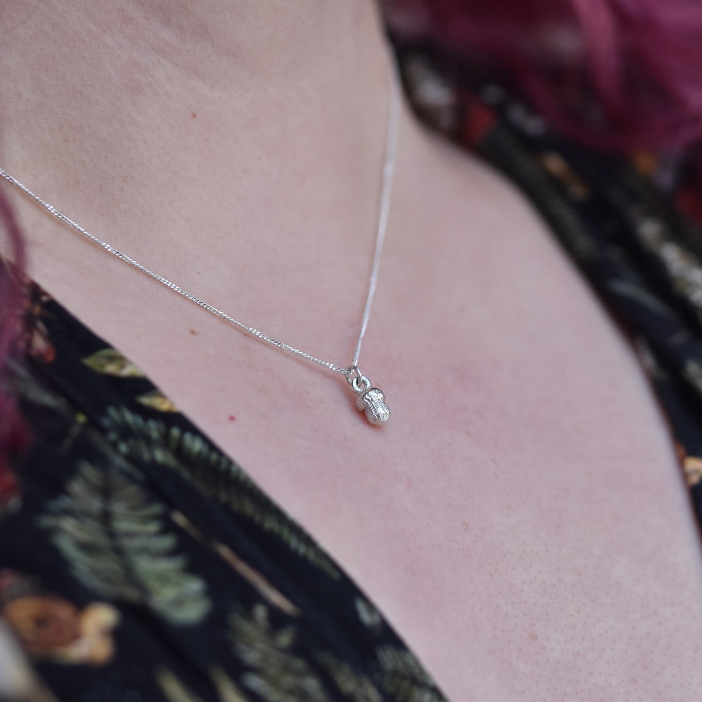 Girl with red hair and dress with mushrooms on is wearing a silver necklace with a tiny realistic acorn