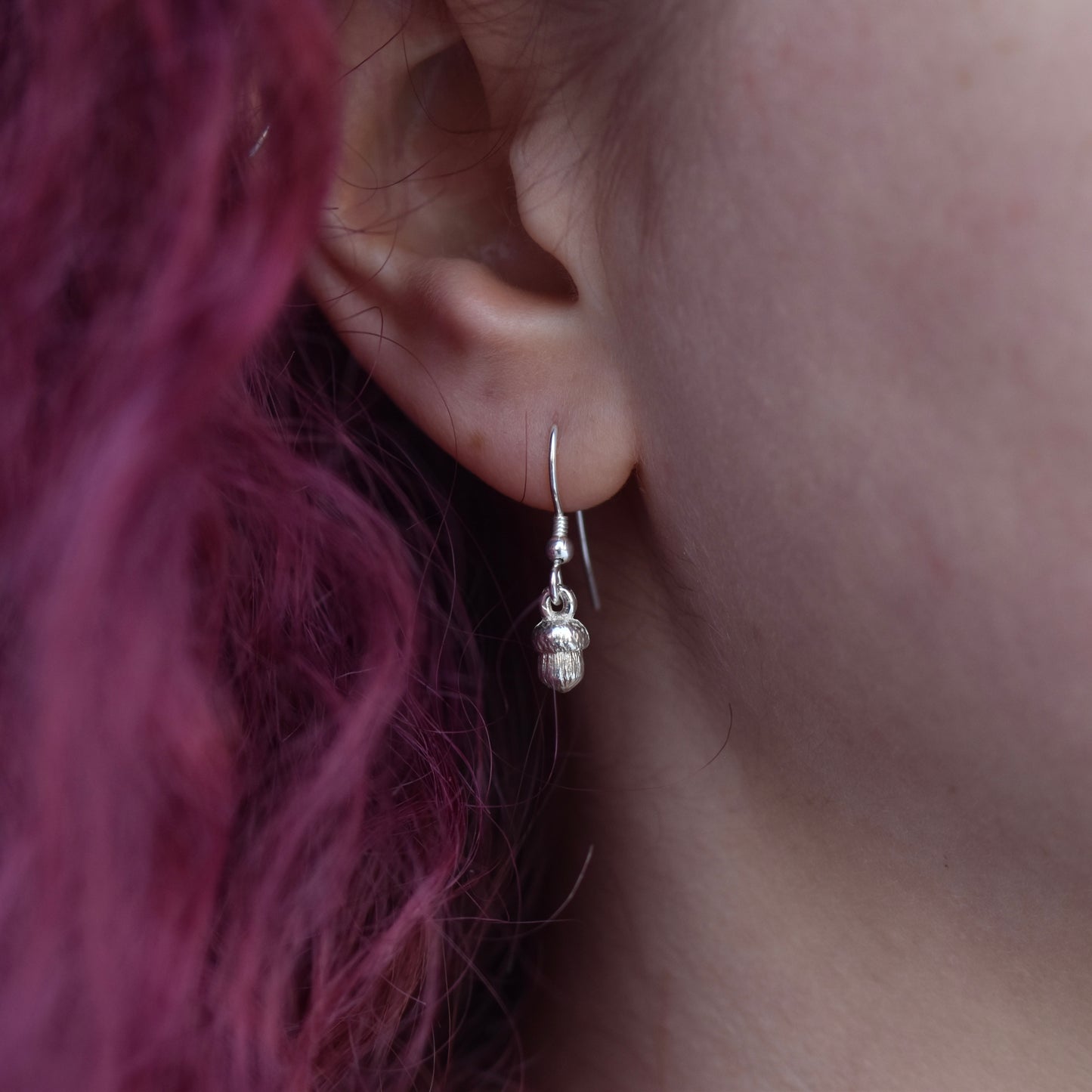 Girl with red hair is wearing a drop earring made of silver. The earring is a tiny silver acorn