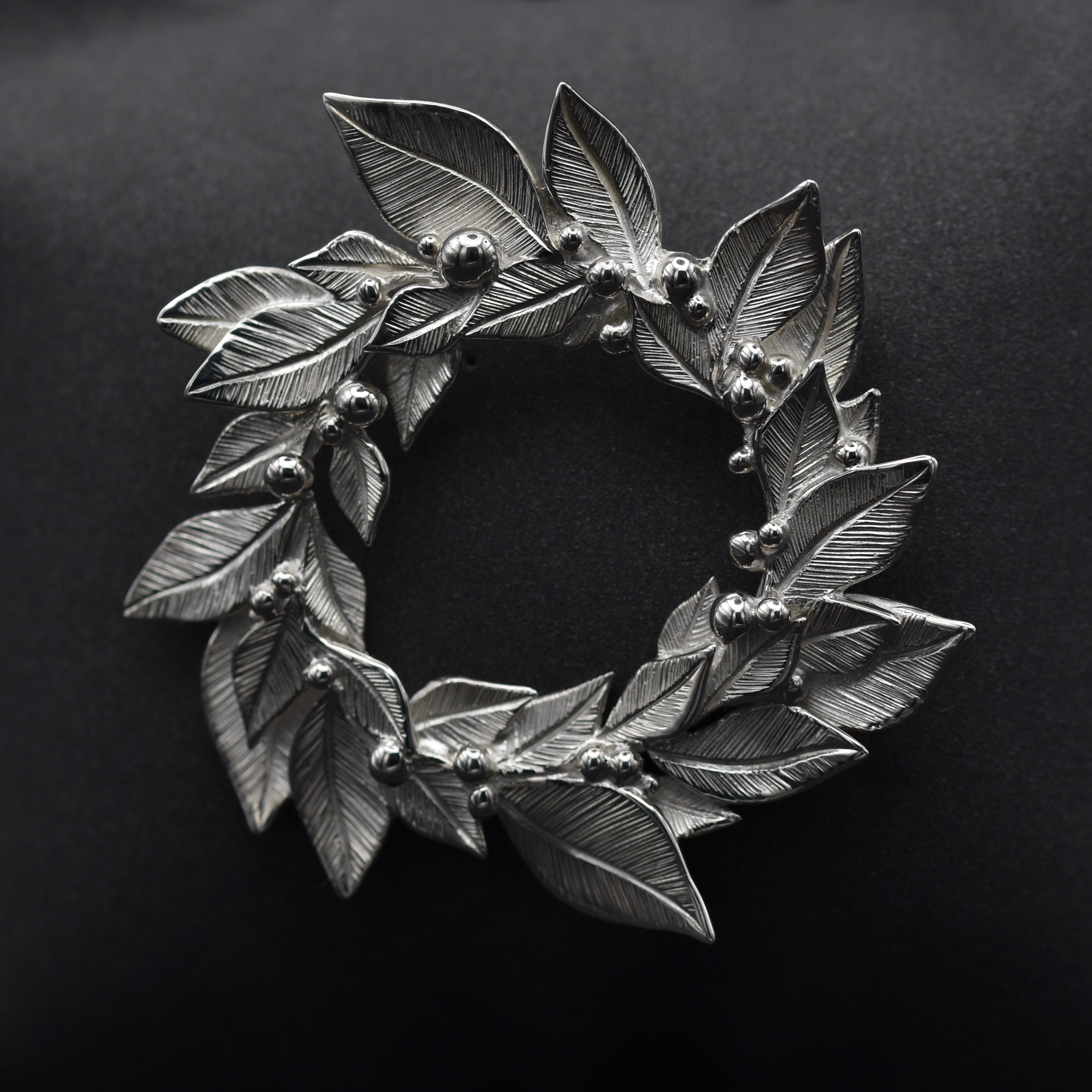 Brooch in the shape of a wreath made from silver with little silve on a black backgroundr granules