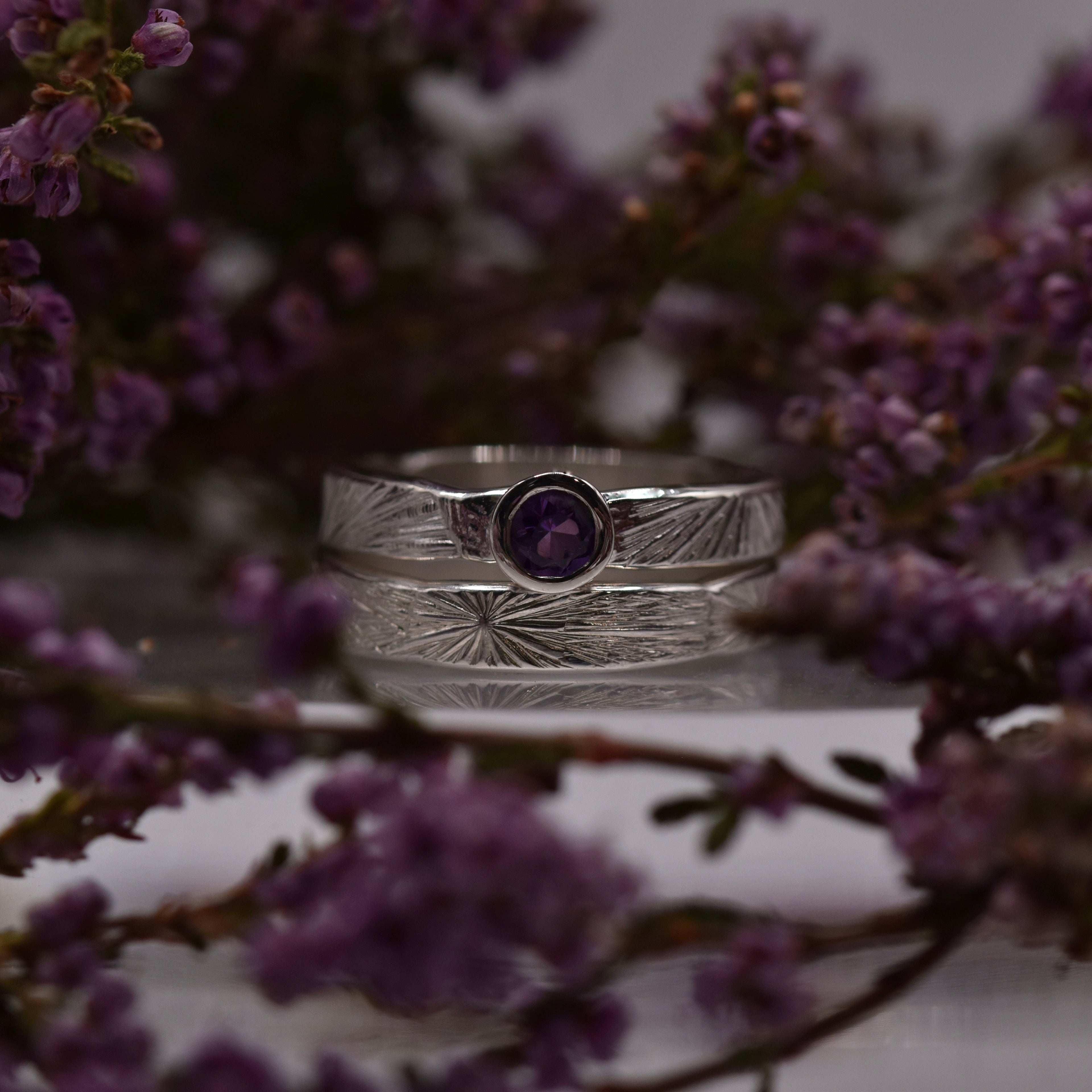 2 Rings stacked, one with an amethyst set in the middle and surrounded by heather