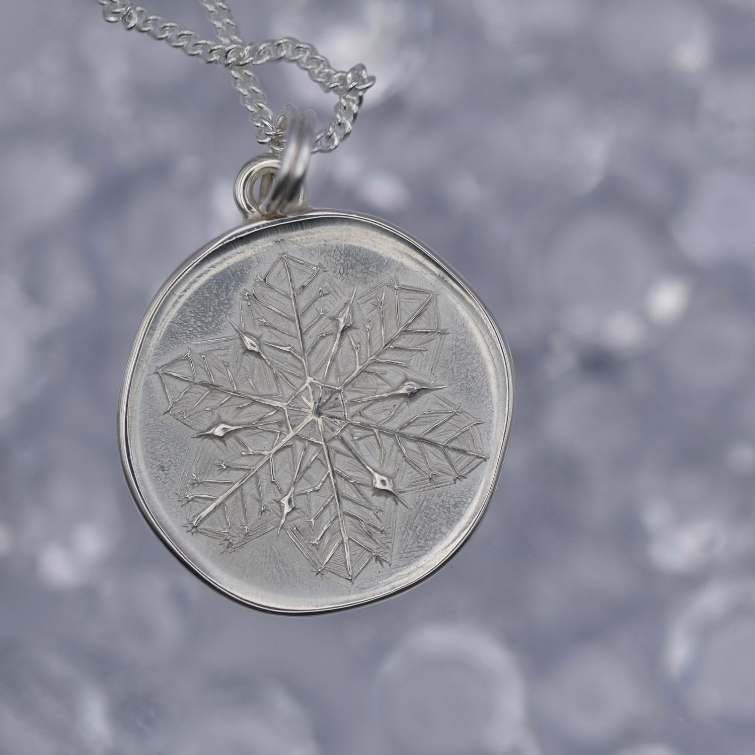 A silver pendant with a depiction of a snowflake 