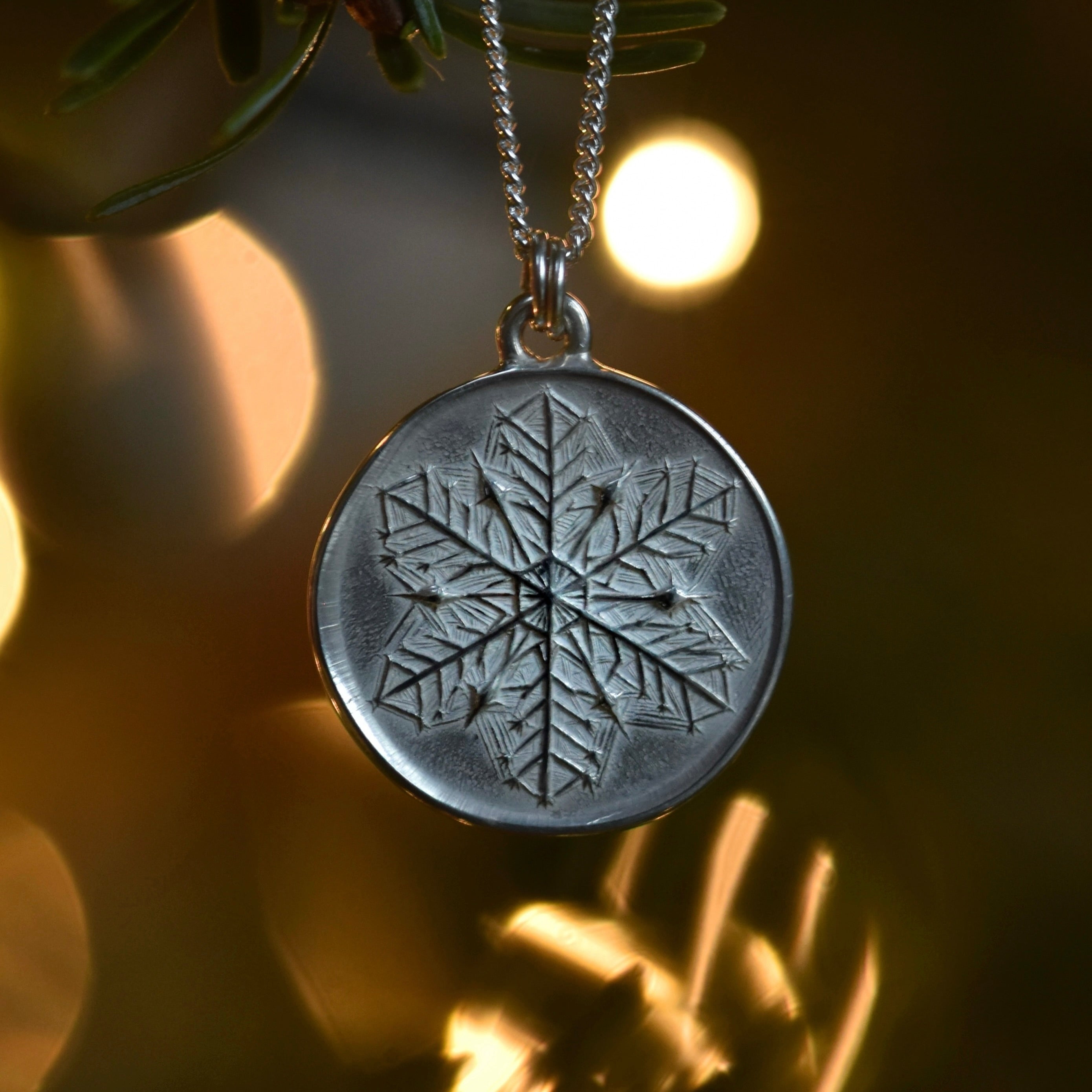 Silver pendant with detailed snowflake motif on bokeh backgorund