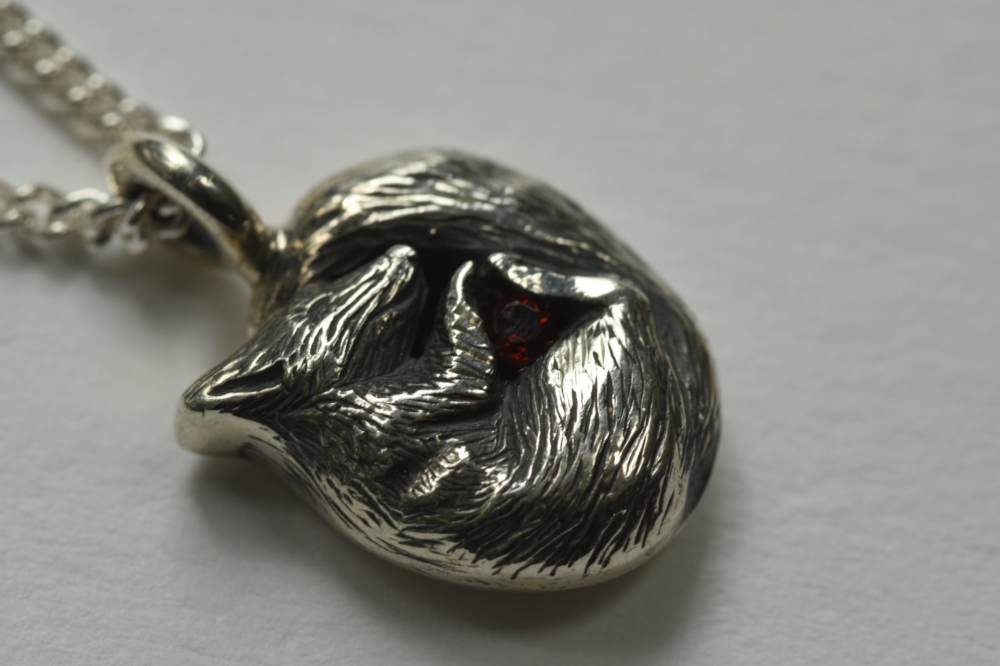 Pendant showing engraved silver squirrel clutching a garnet hanging from a silver chain worn by a girl with a red top and red hair.