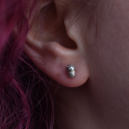 Girl with red hair is wearing a small silver acorn stud earring