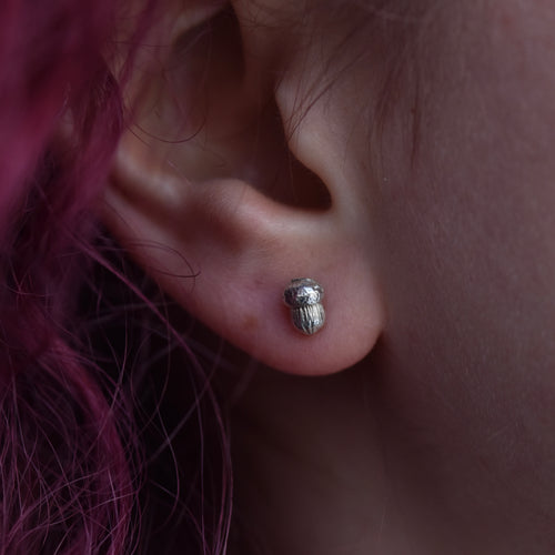 Girl with red hair is wearing a small silver acorn stud earring