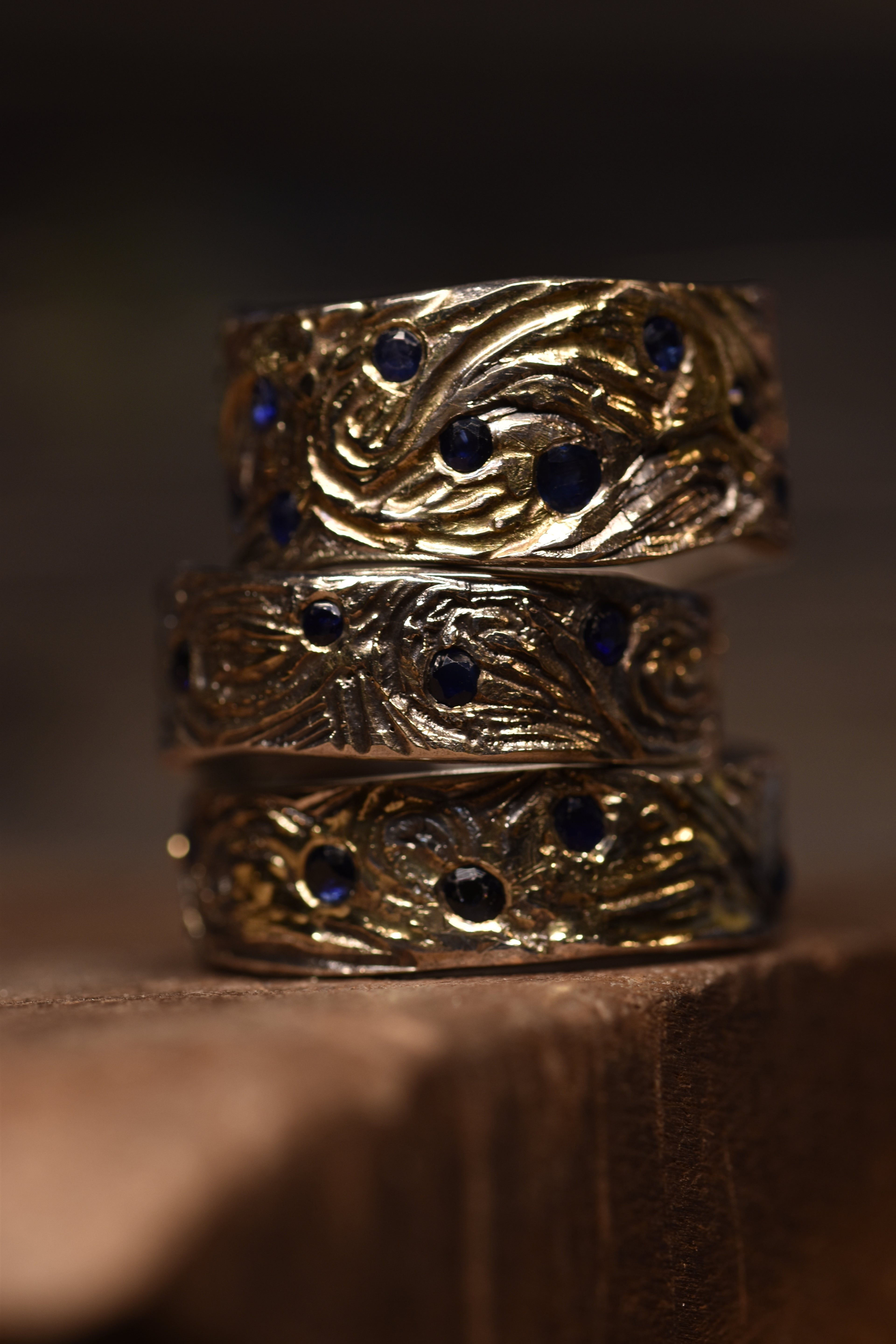 A stack of silver and gold rings with hand engraved patterns set with blue sapphire stones