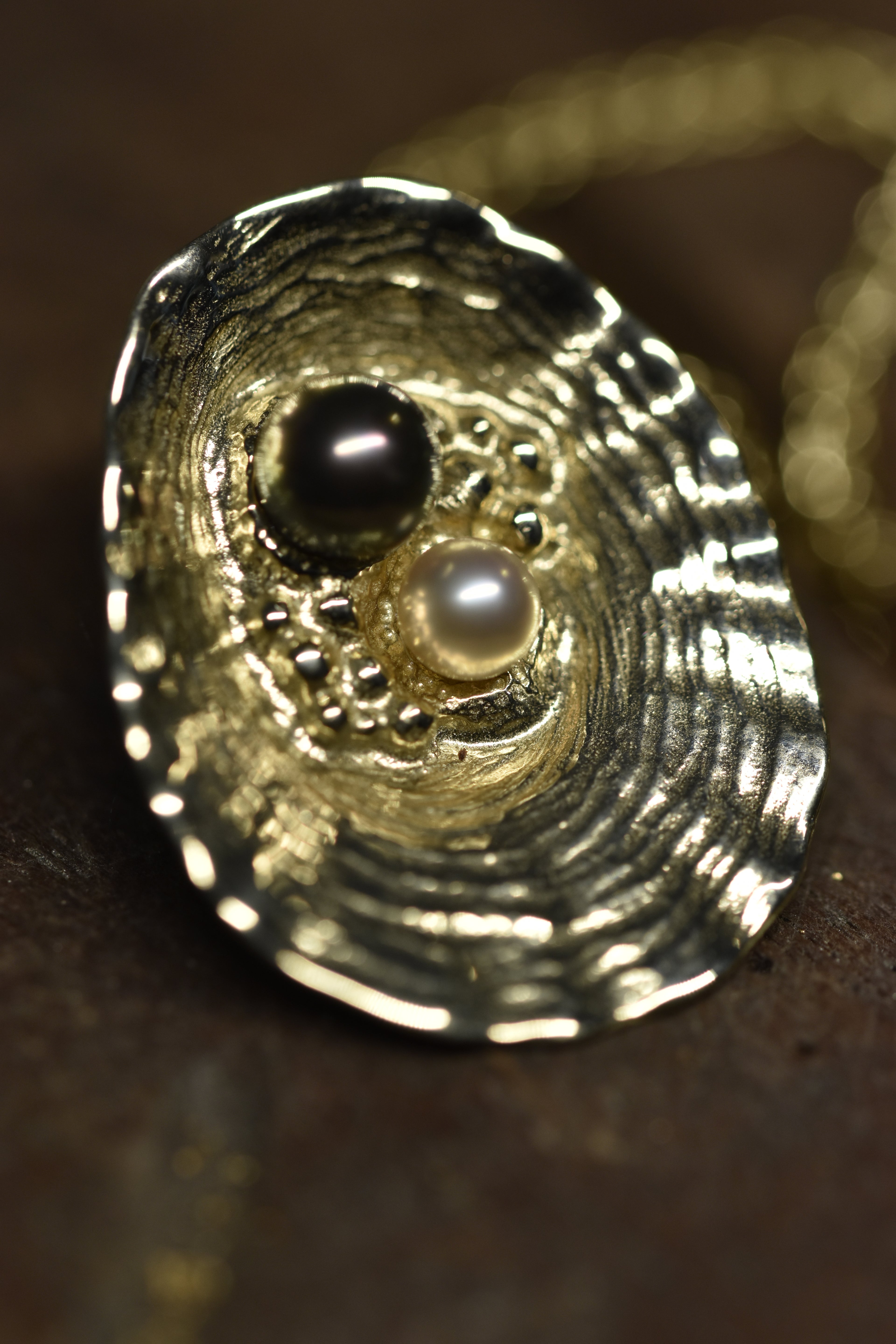 Close-up of a gold shell pendant with black and white pearls on a dark background
