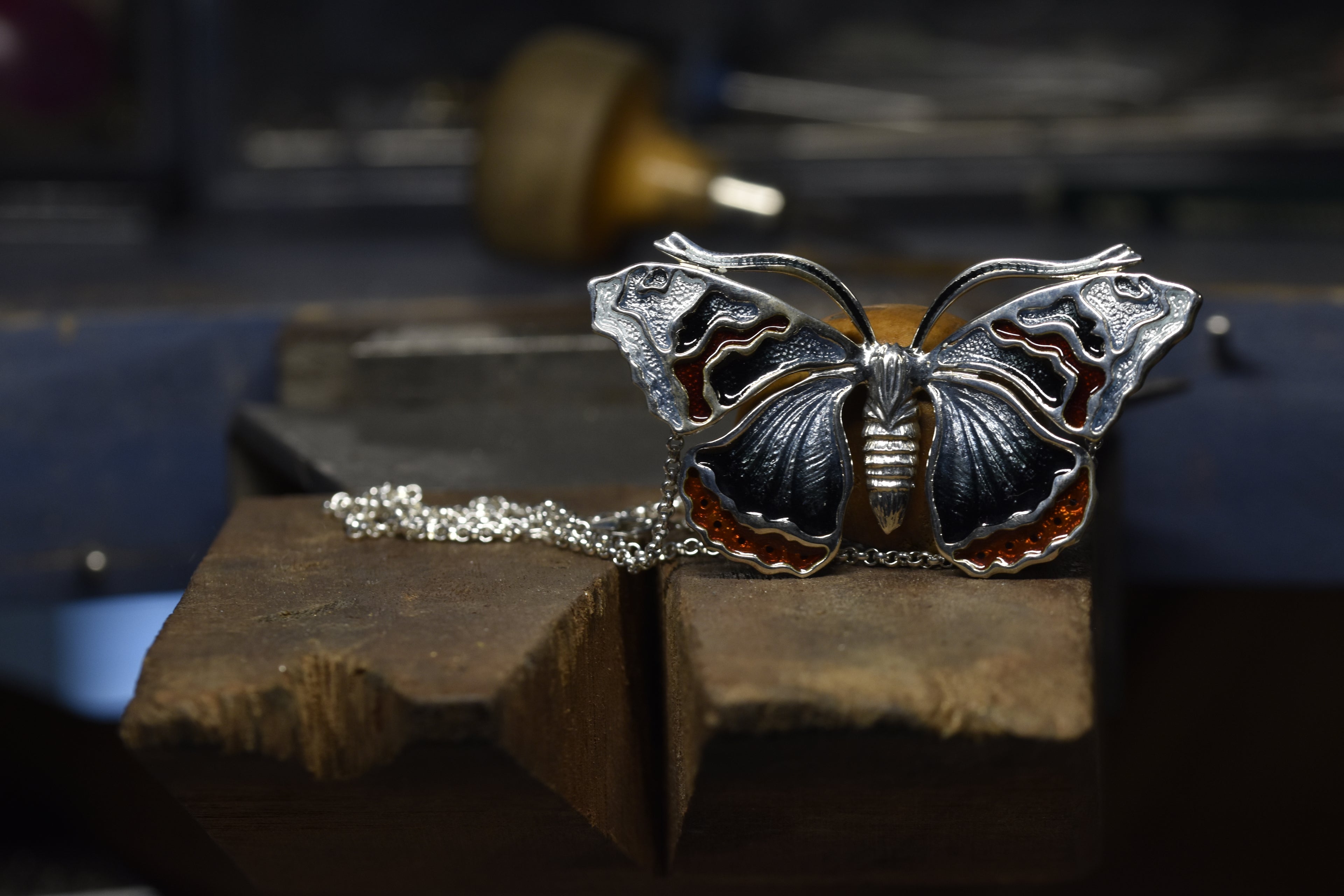 Red admiral Butterfly-shaped silver pendant on a wooden block with a blurred background