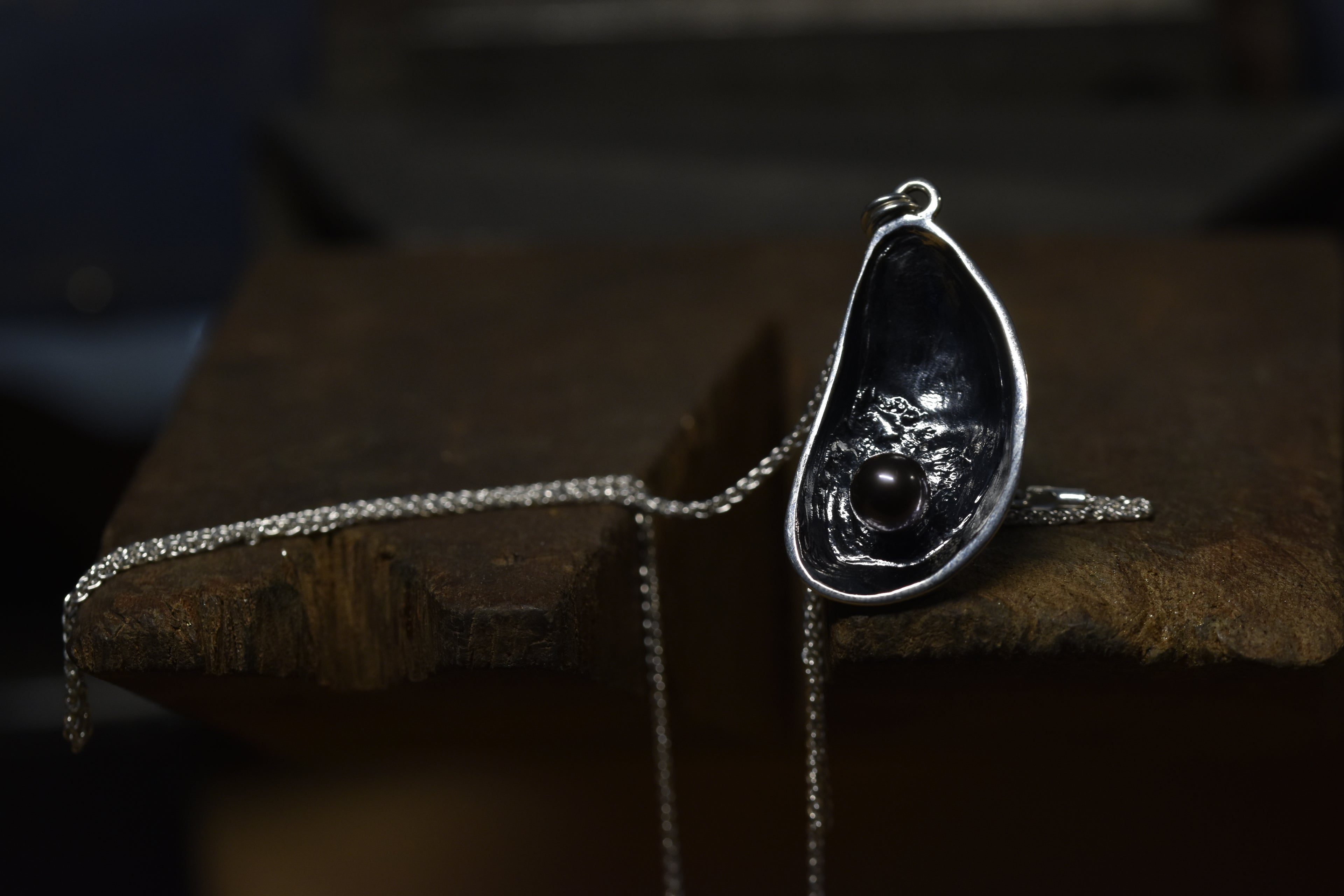 Silver mussel shell pendant with black pearl on a dark wooden surface
