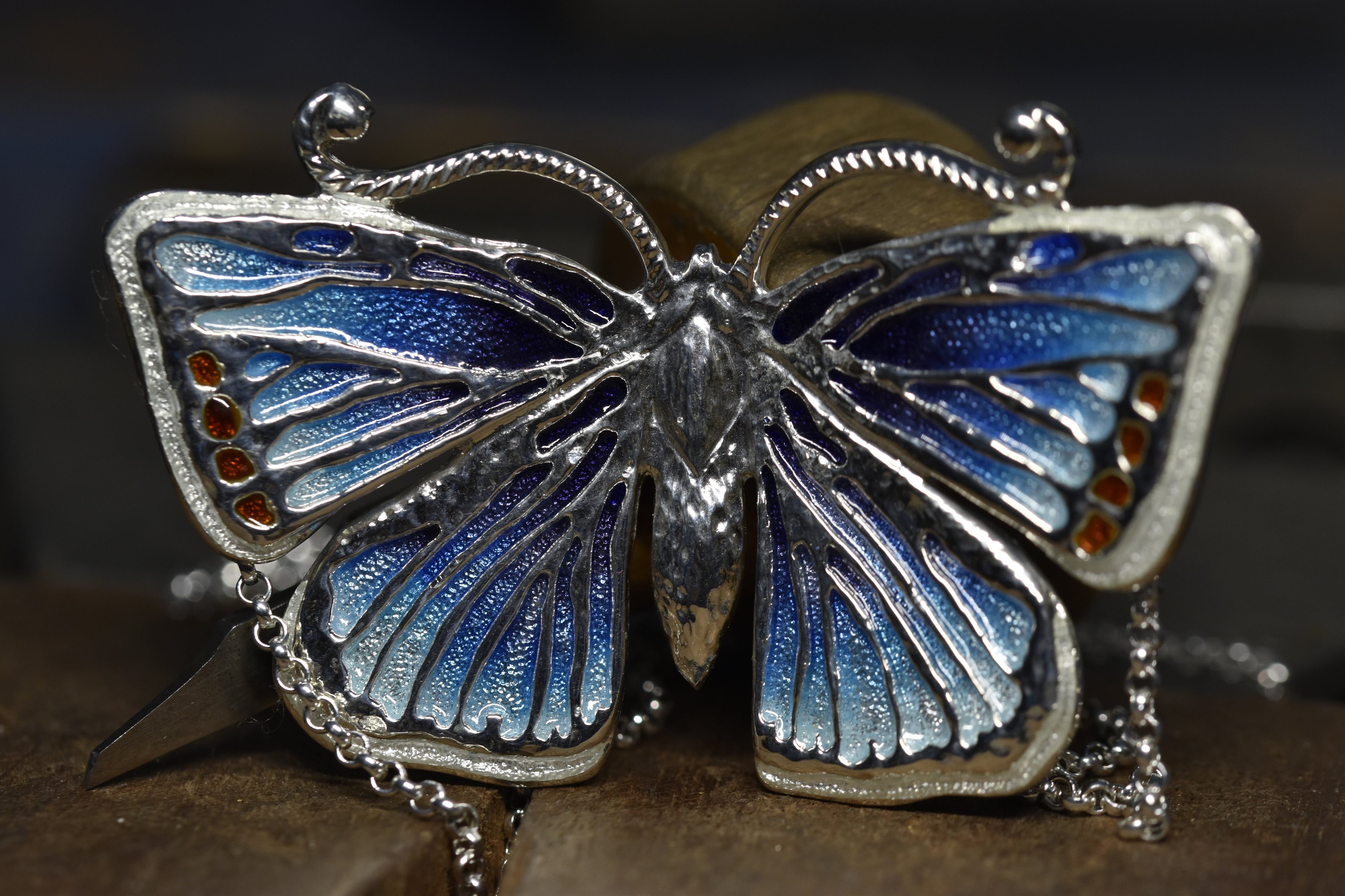 Butterfly-shaped necklace with blue and silver enamel on a dark background