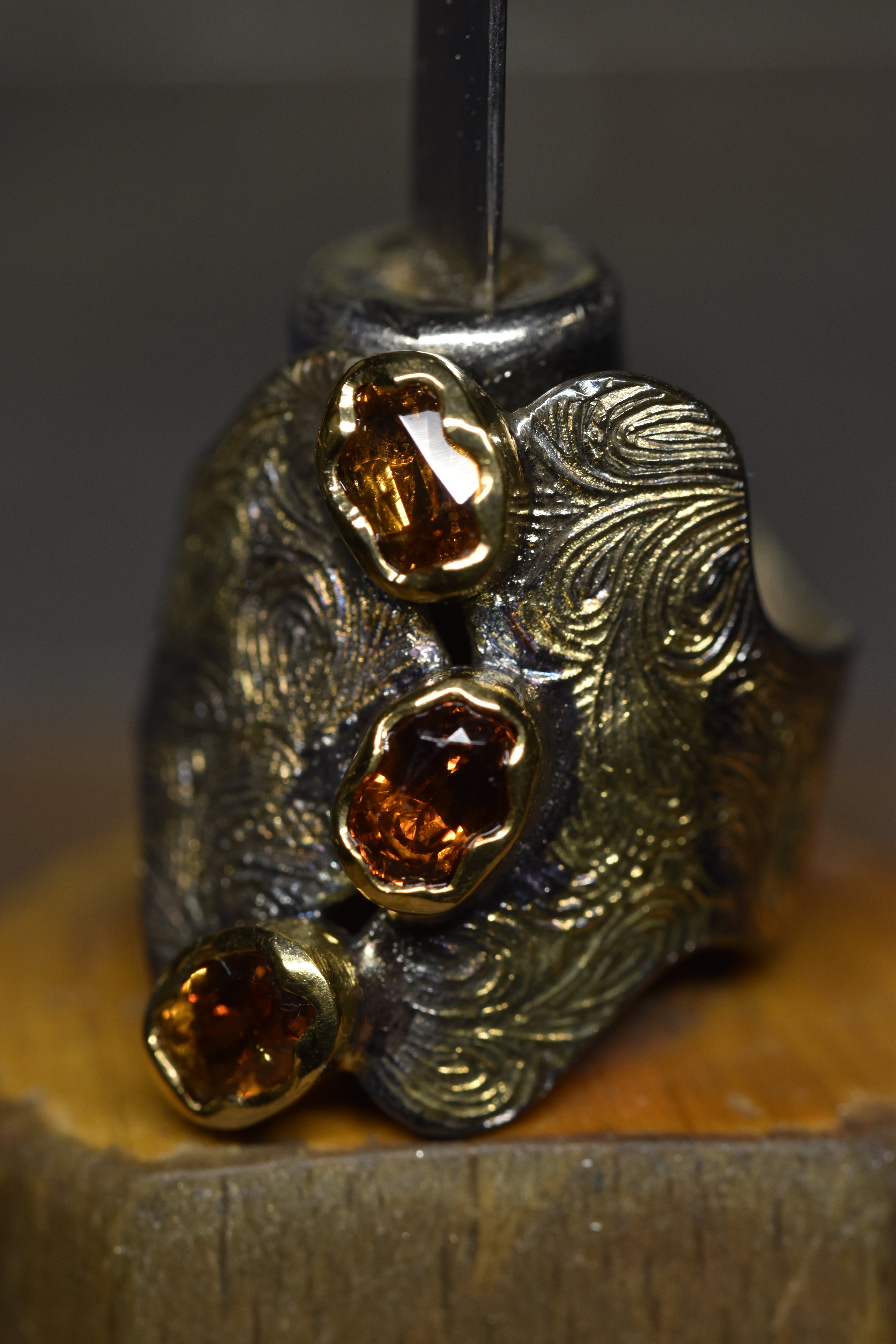 Close-up of a decorative  silver and gold ring with orange garnet stones on a wooden surface.