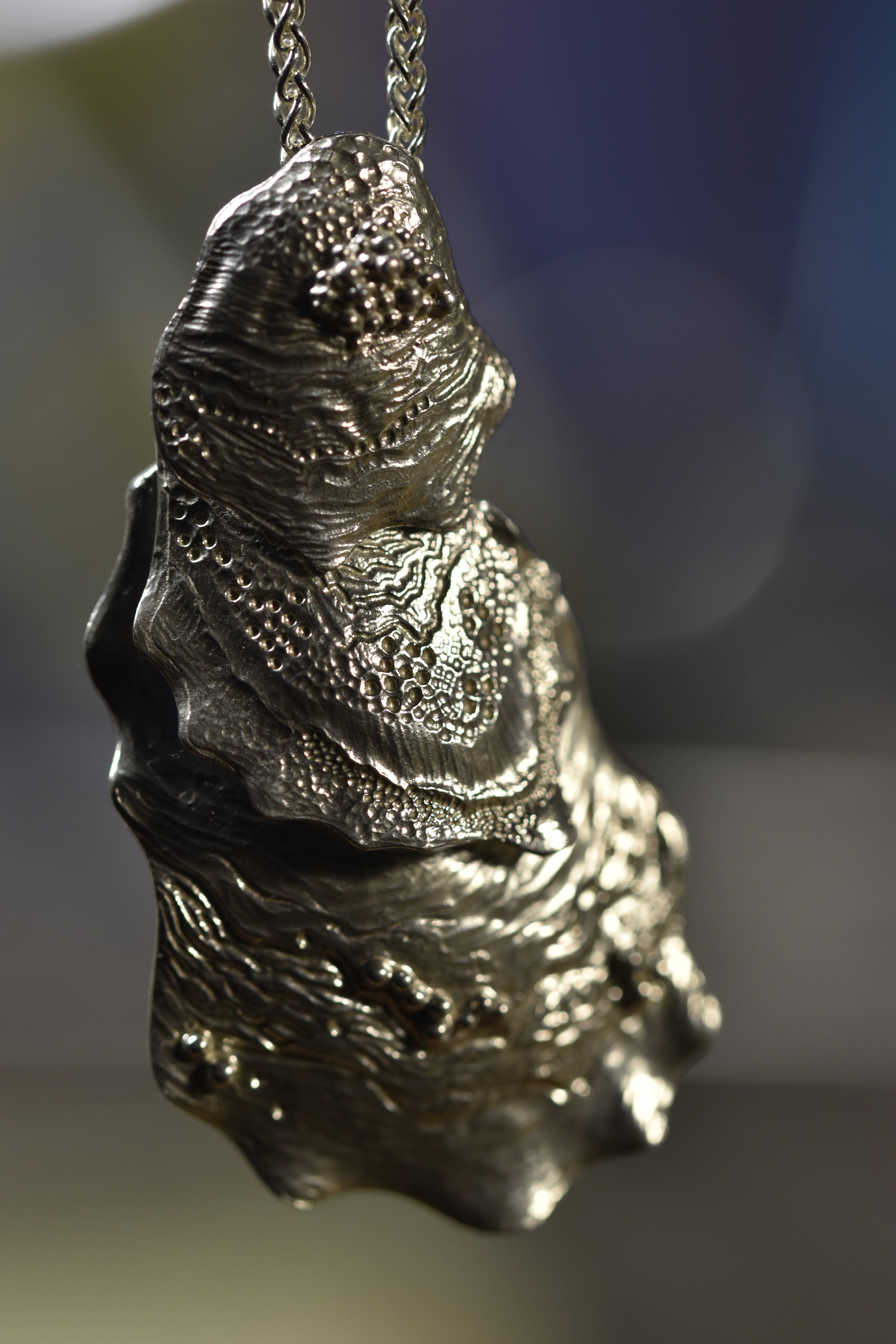 silver pendant with intricate engraving on a chain against a blurred background