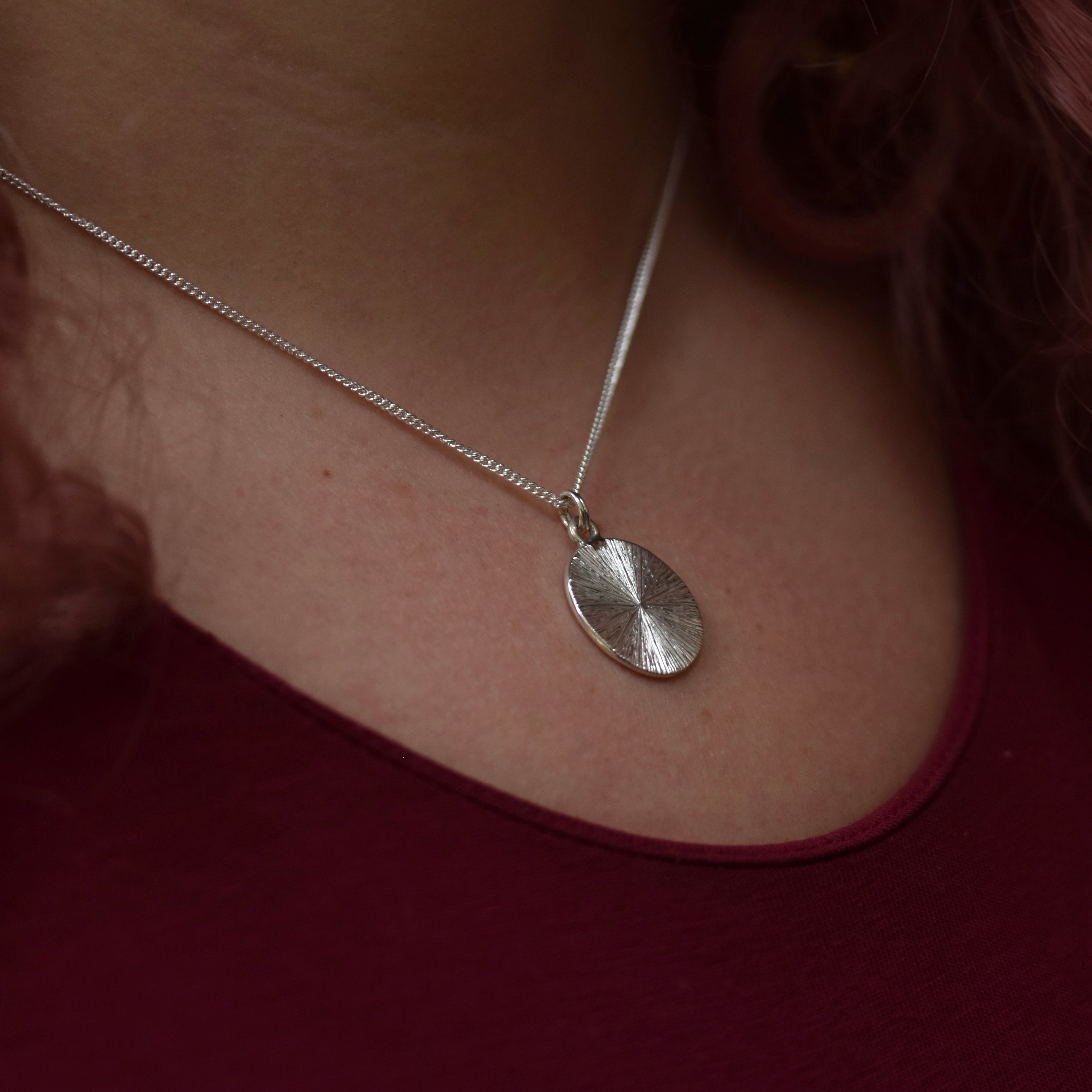 Silver necklace with a round pendant worn by a person 