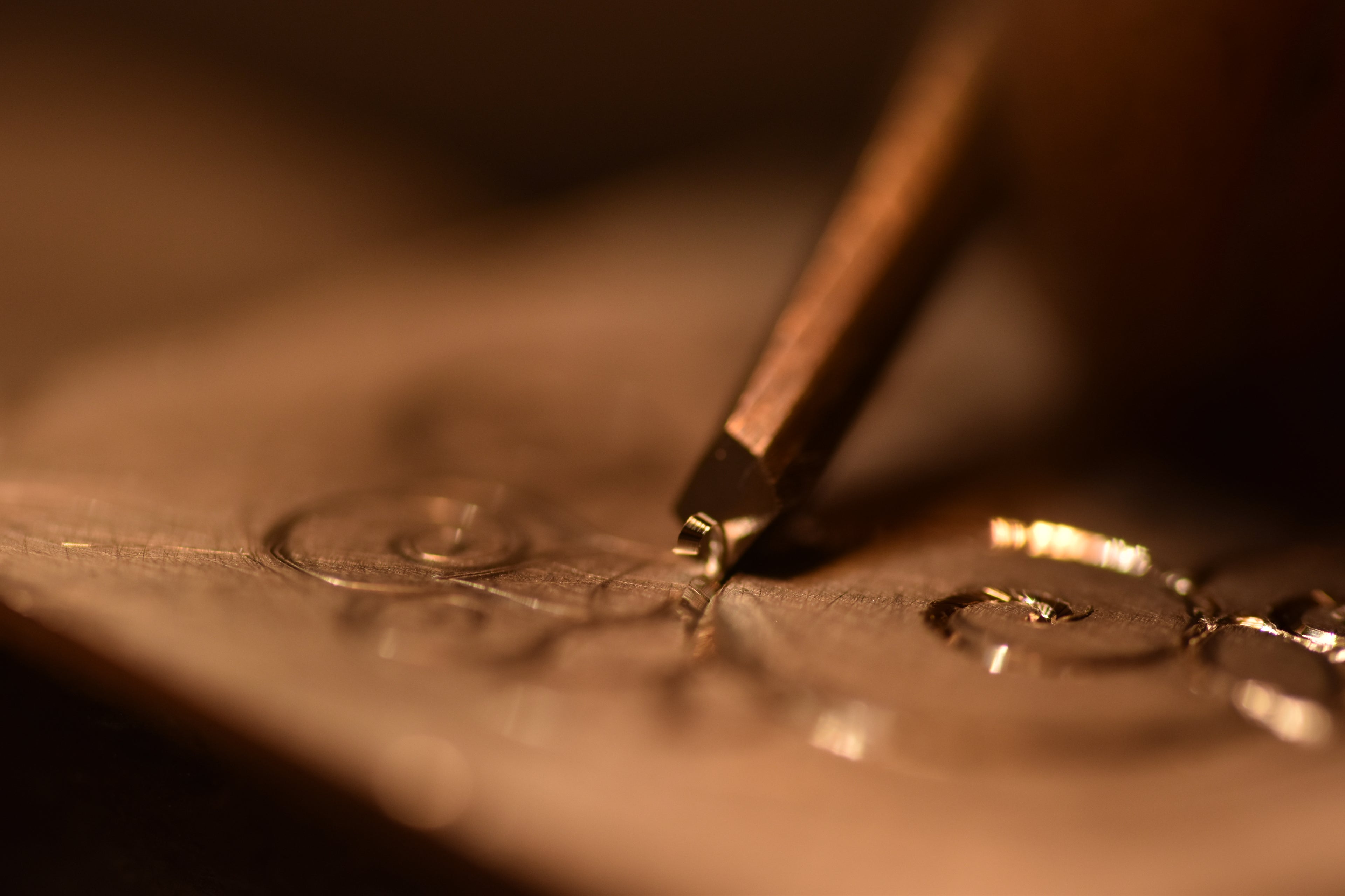 close up of a graver hand cutting a spiral pattern in silver