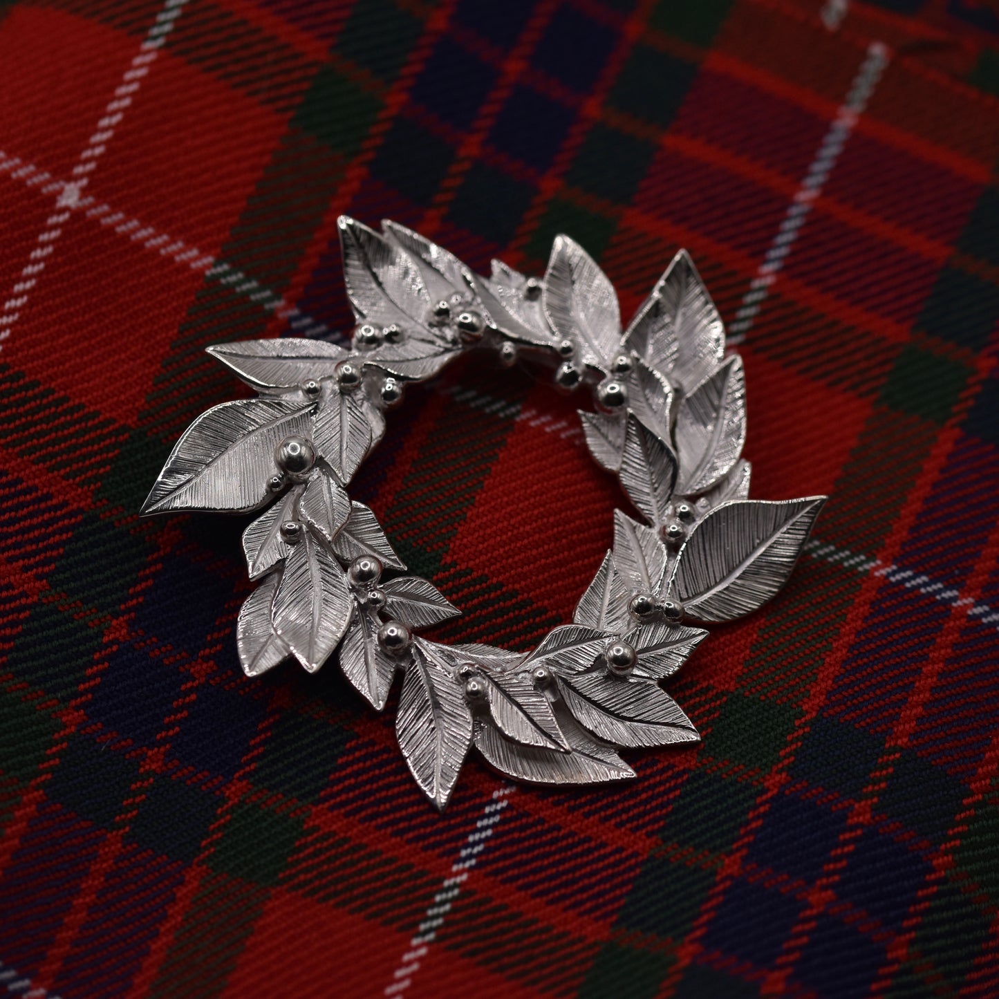 Silver leaf-shaped brooch on a red and black plaid fabric background