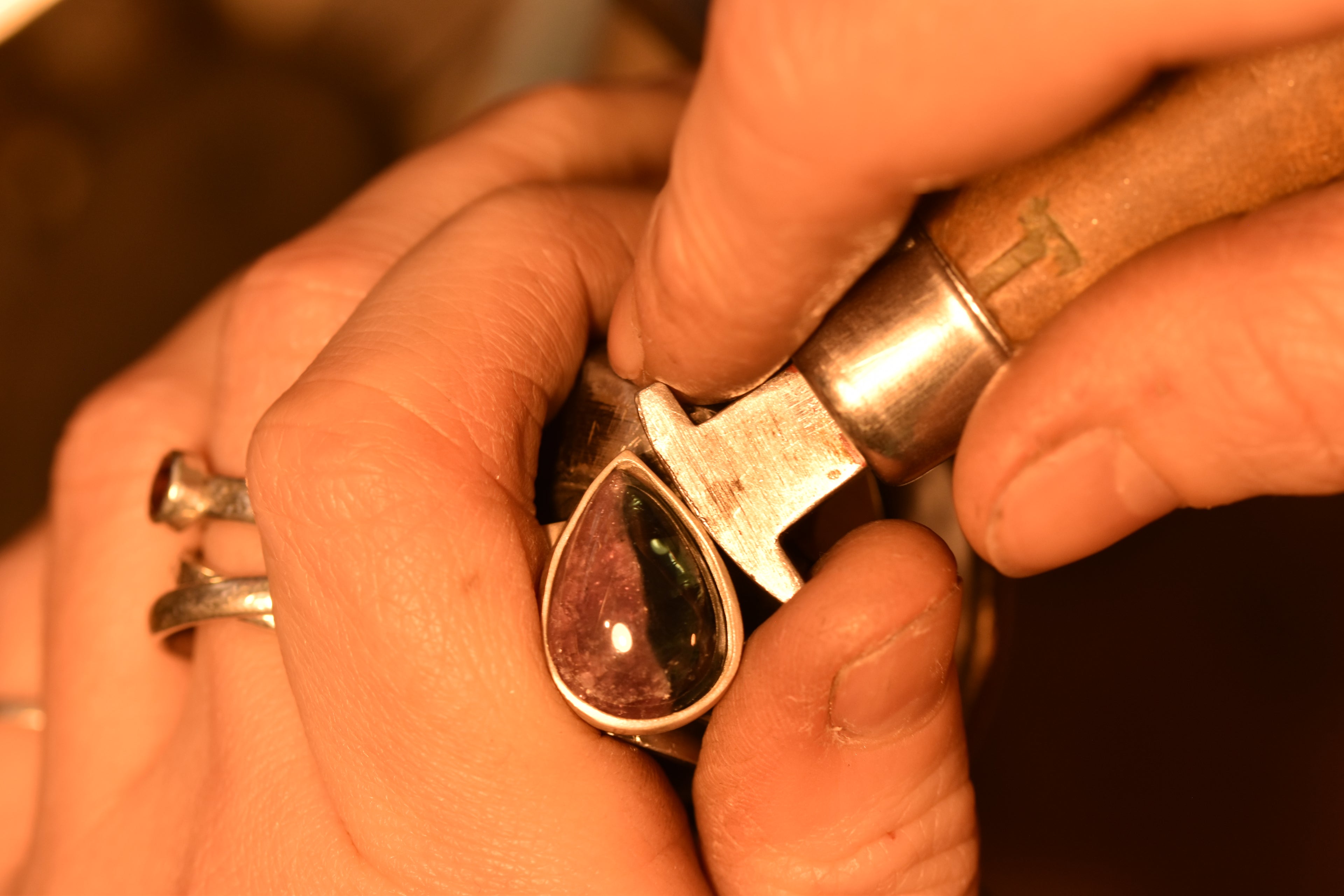 Close-up of hands working on a piece of jewelry with a teardrop-shaped gemstone.