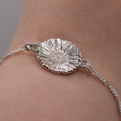 Silver bracelet with a daisy shaped motif on a wrist against a neutral background