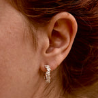 Close-up of an ear wearing a flower covered hoop earring with hair partially covering the frame.