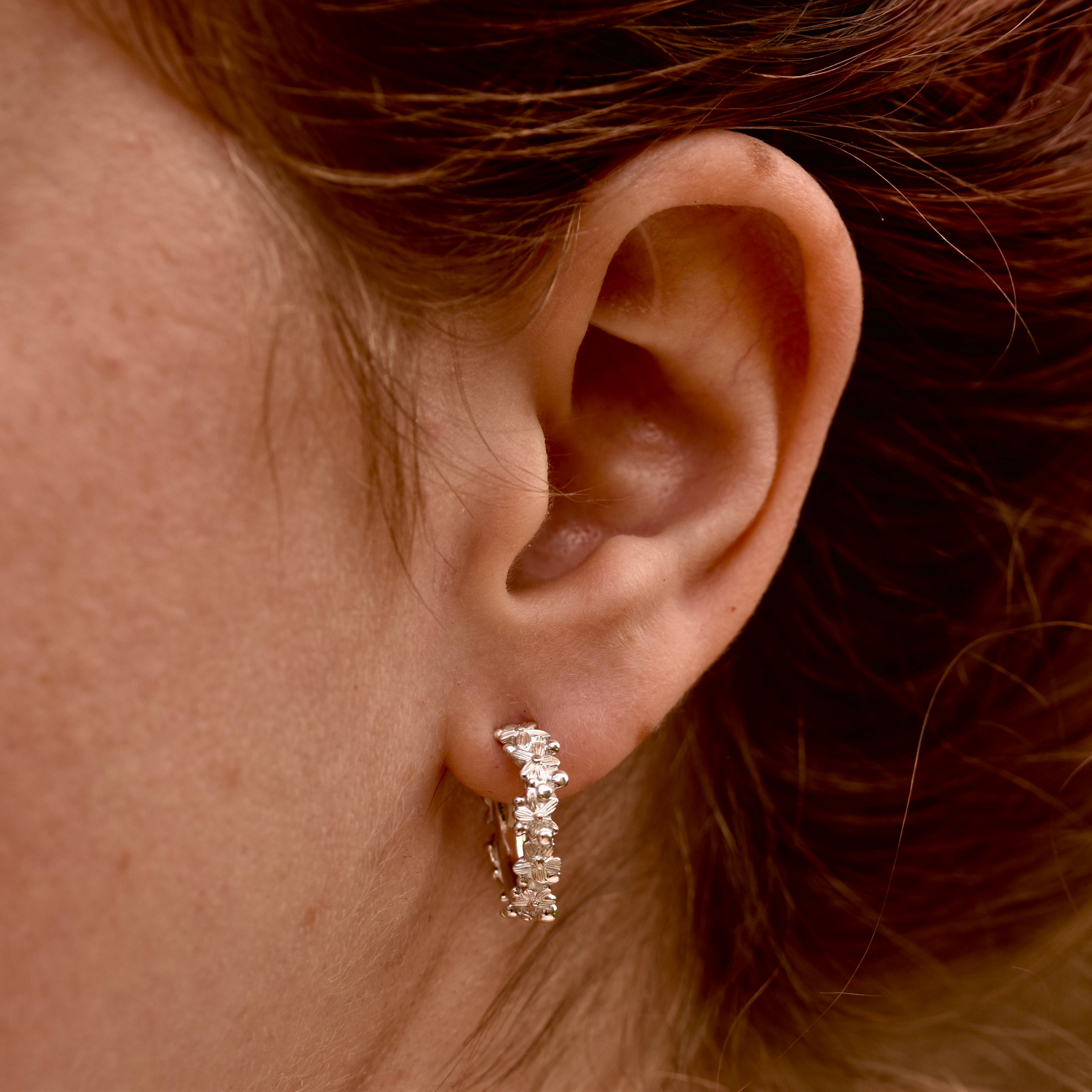 Close-up of an ear wearing a flower covered hoop earring with hair partially covering the frame.