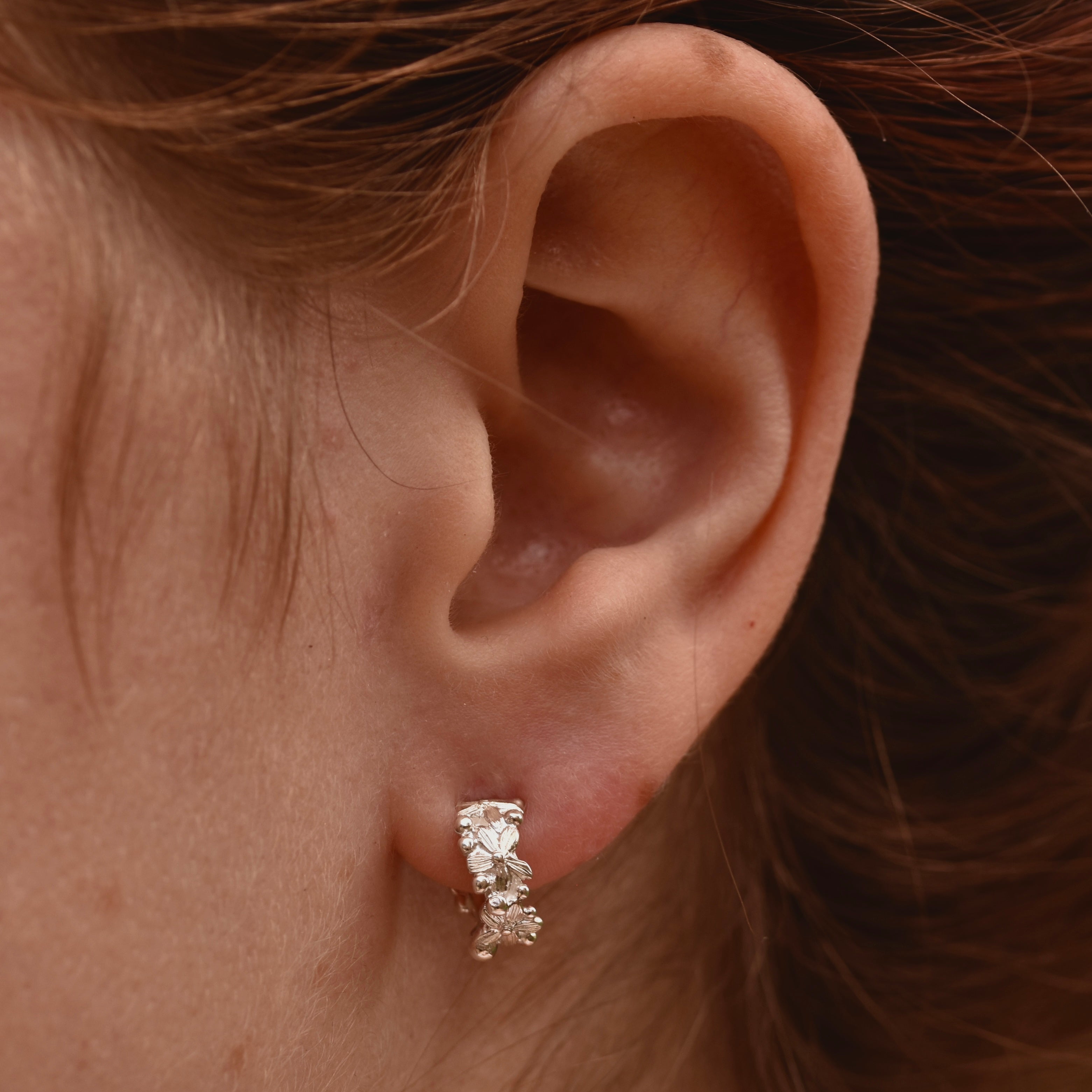 Close-up of an ear wearing a flower covered hoop earring with hair partially covering the frame.