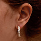 Close-up of an ear wearing a flower covered hoop earring with hair partially covering the frame.