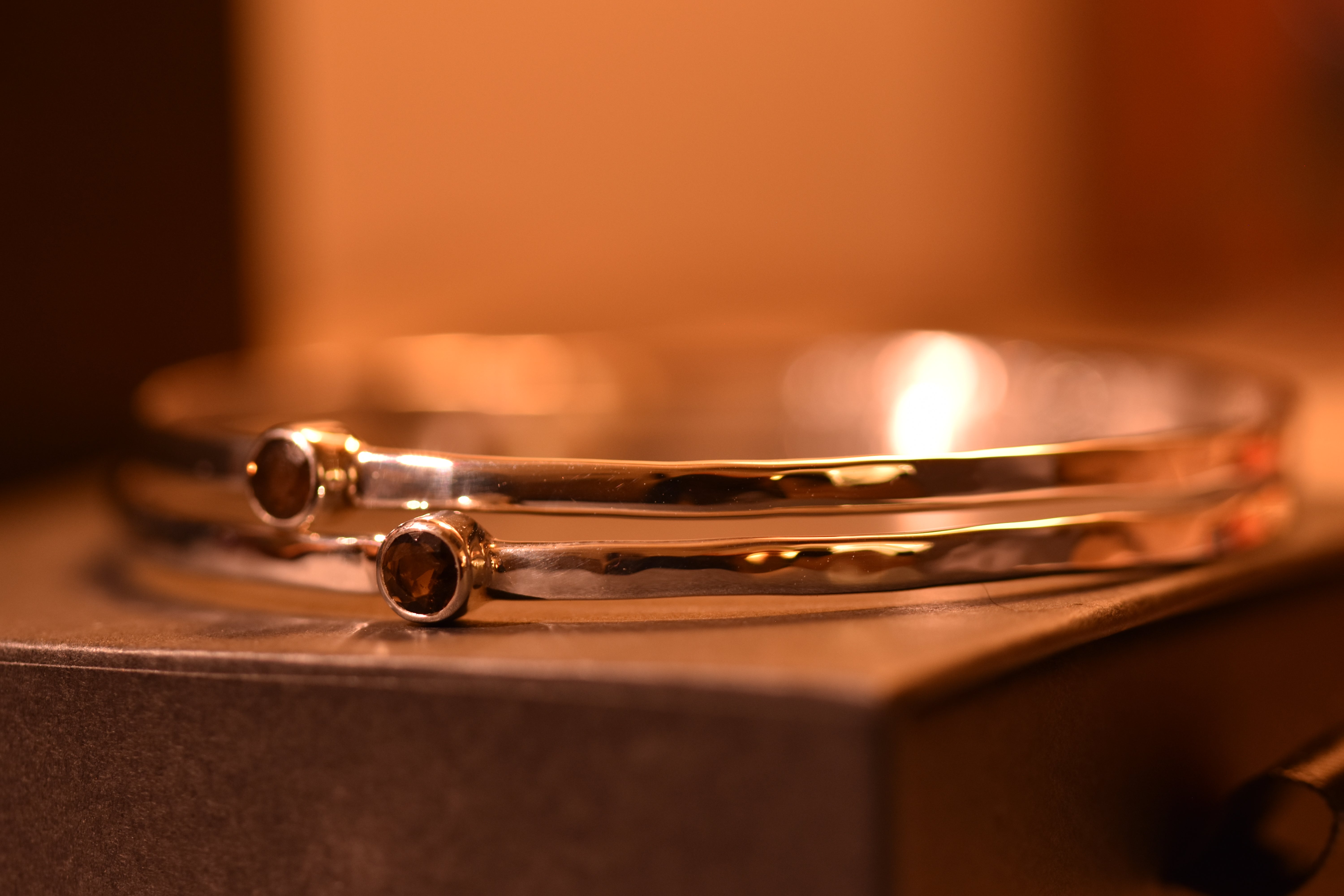 Two silver bangles with smokey quartz on a wooden surface with a warm, blurred background