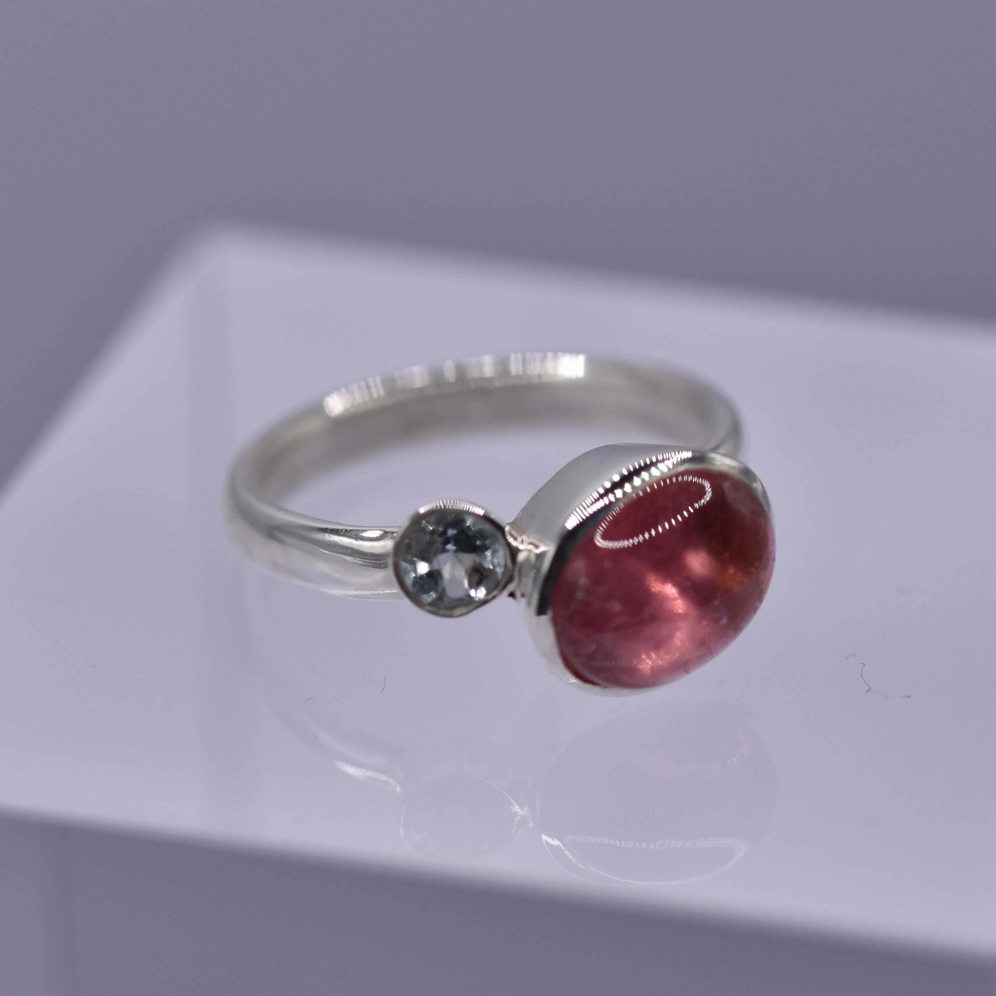 Silver ring with a pink gemstone and a blue gemstone on a white platform