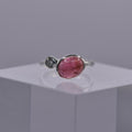 Silver ring with a pink gemstone beside a blue gemstone on a gray background