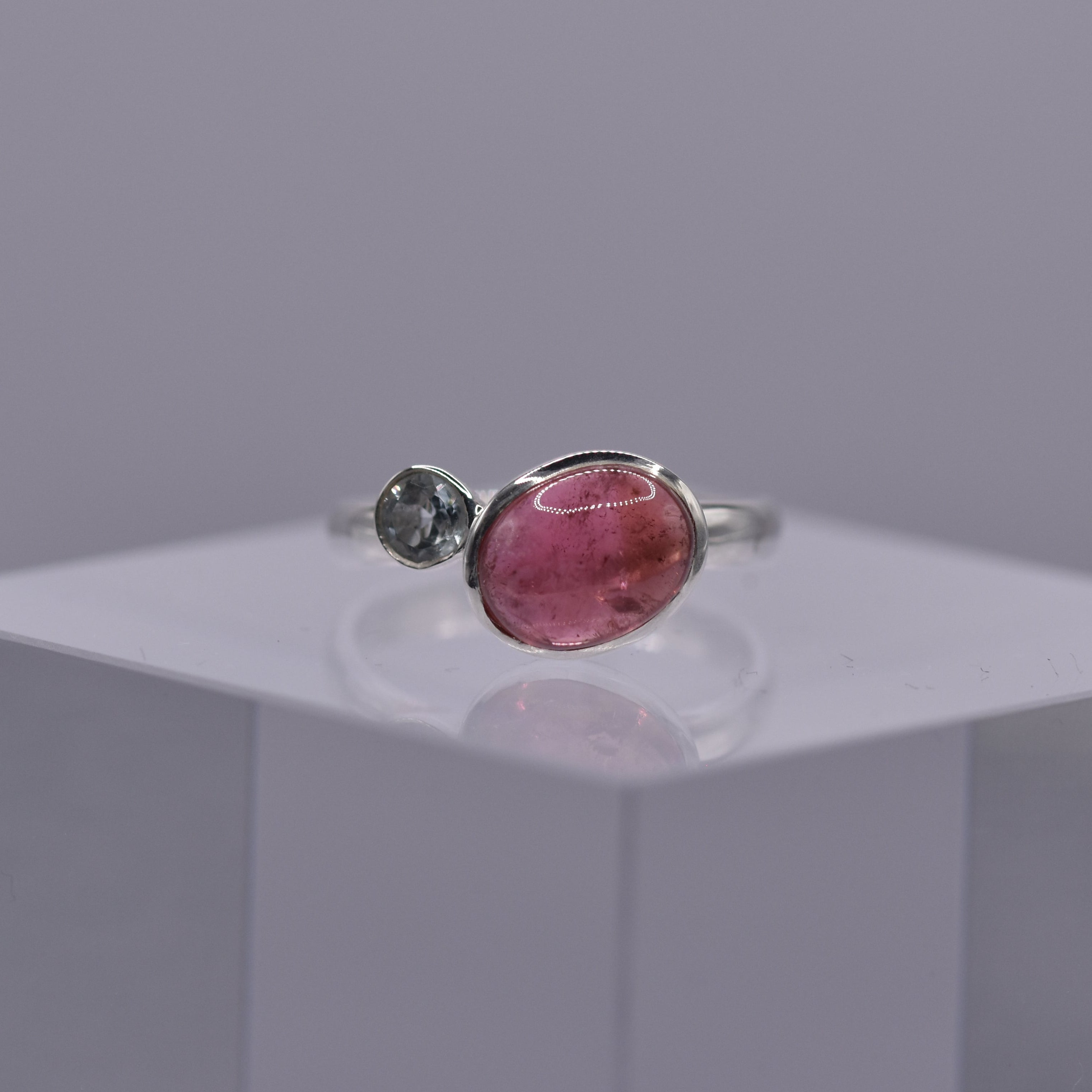 Silver ring with a pink gemstone beside a blue gemstone on a gray background