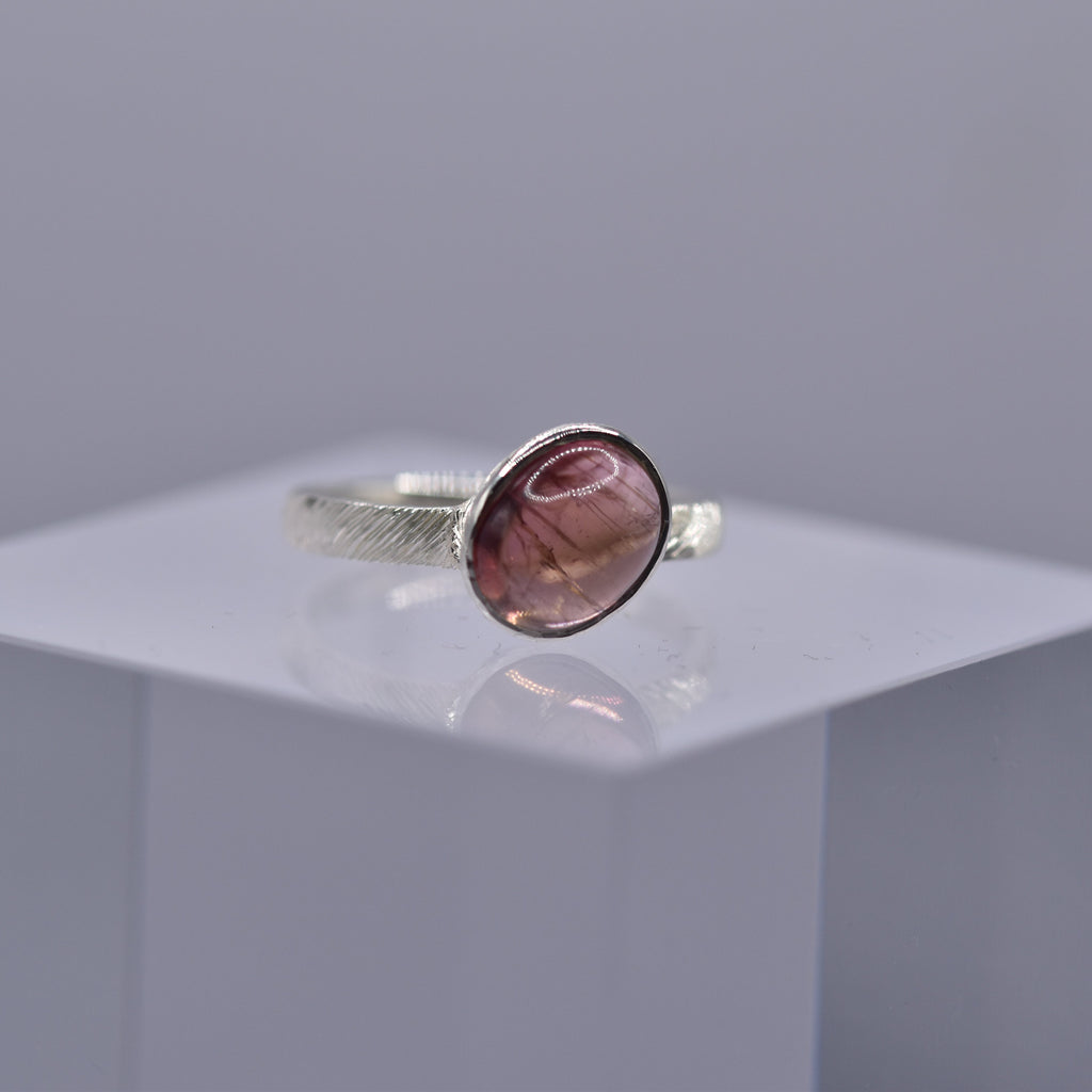 Silver ring with a pinkish-purple stone on a clear cube with a gray background