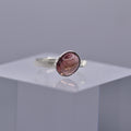 Silver ring with a pinkish-purple stone on a clear cube with a gray background