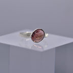 Silver ring with a pinkish-purple stone on a clear cube with a gray background