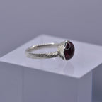 Silver ring with a pinkish gemstone with textured hand engraved lines on a clear cube against a gray background