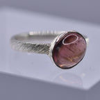 Silver ring with a pink stone on a clear stand against a gray background