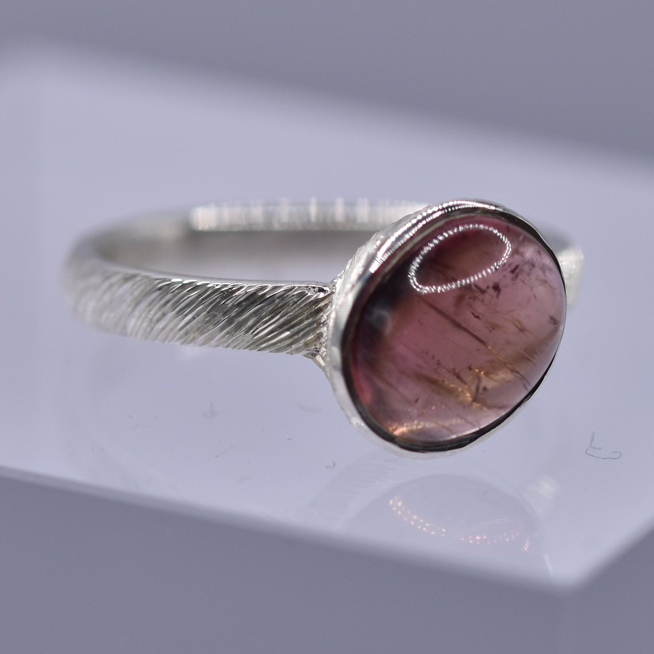 Silver ring with a pink stone on a clear stand against a gray background