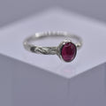 Silver ring with a pink gemstone with swirls and waves engraved on the ring on a gray background