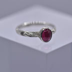 Silver ring with a pink gemstone with swirls and waves engraved on the ring on a gray background